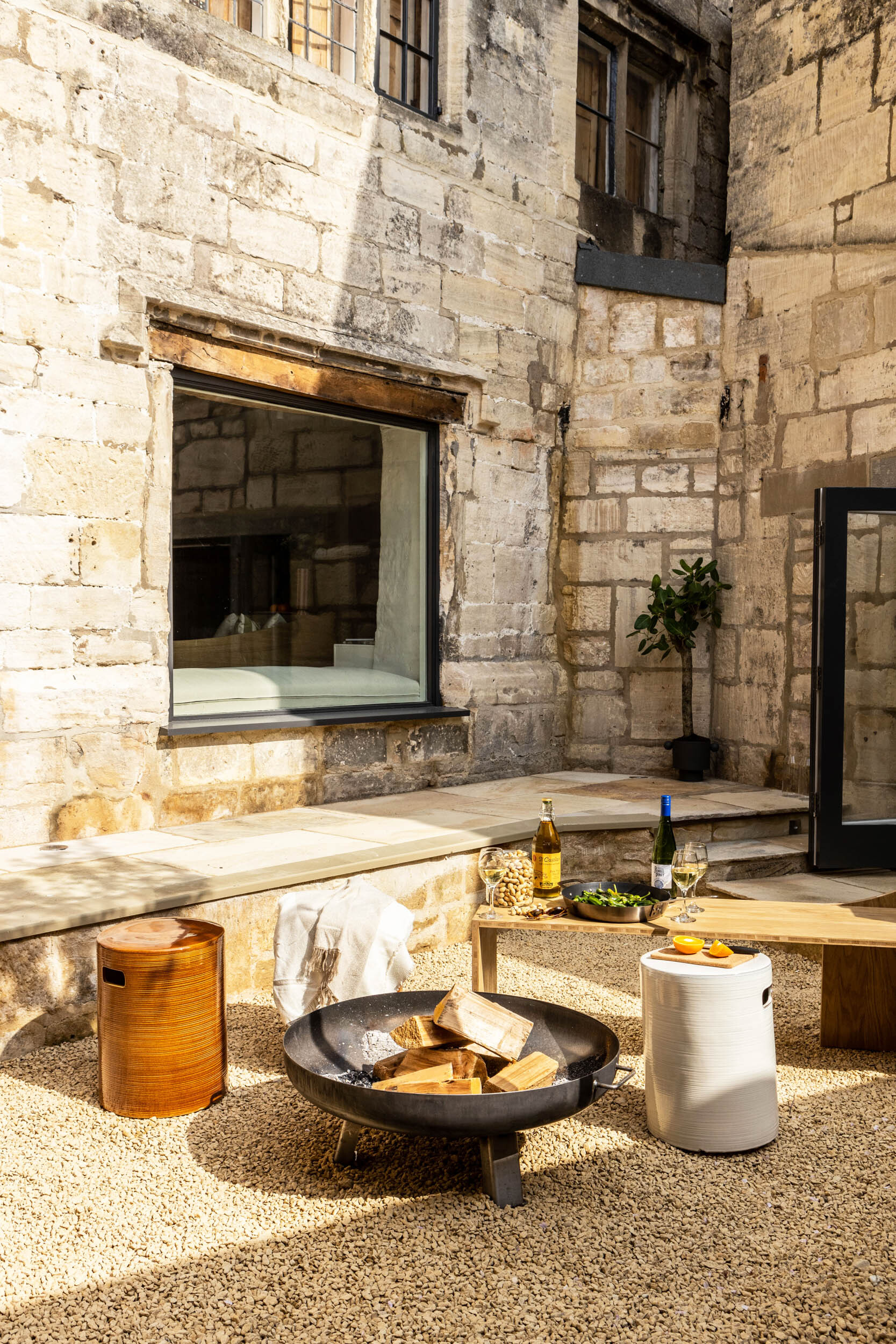 Outdoor terrace with fire bowl and seating framed by weathered stone walls in afternoon sunlight