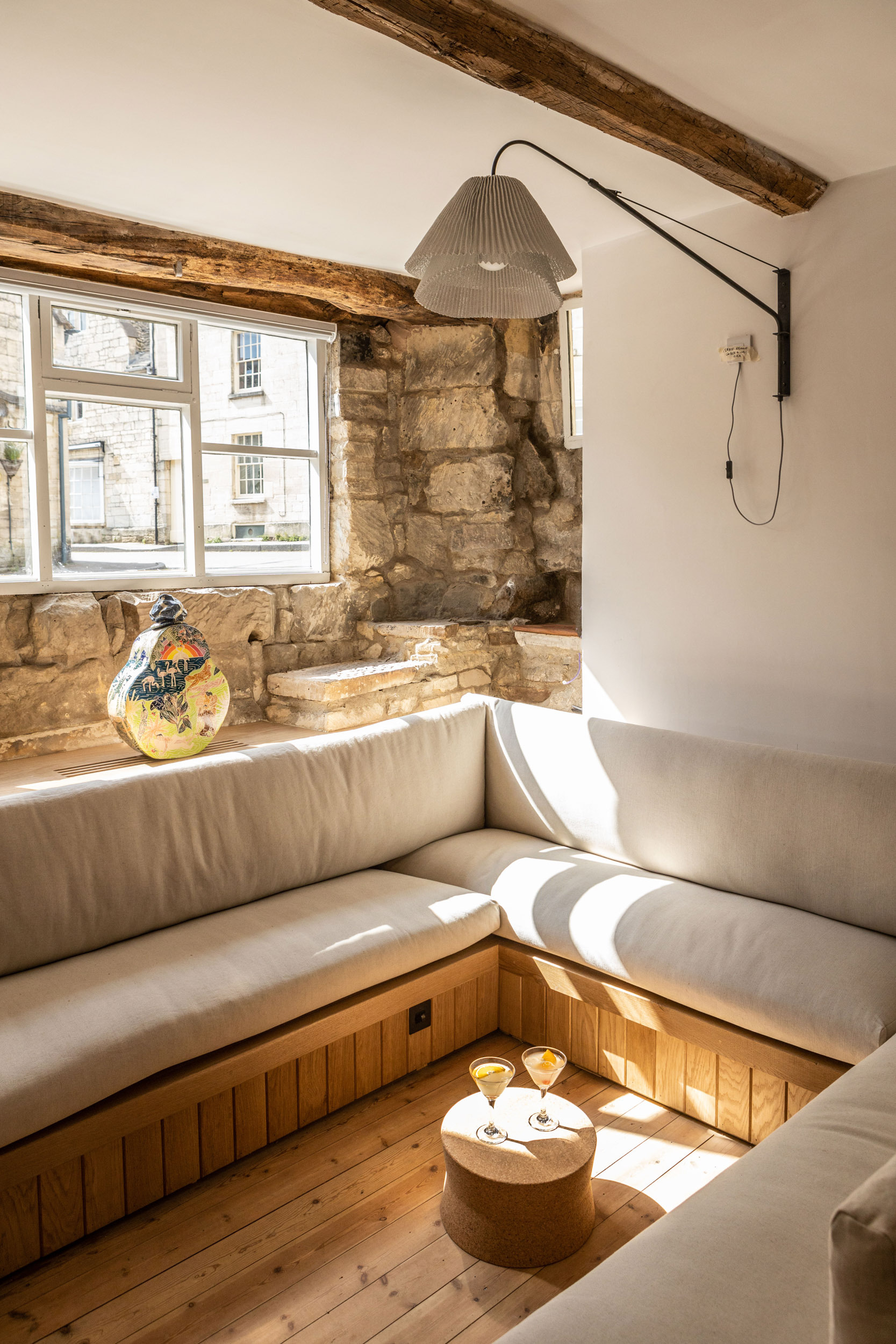 Sunken seating area with upholstered benches and exposed timber beams beside a window overlooking the street