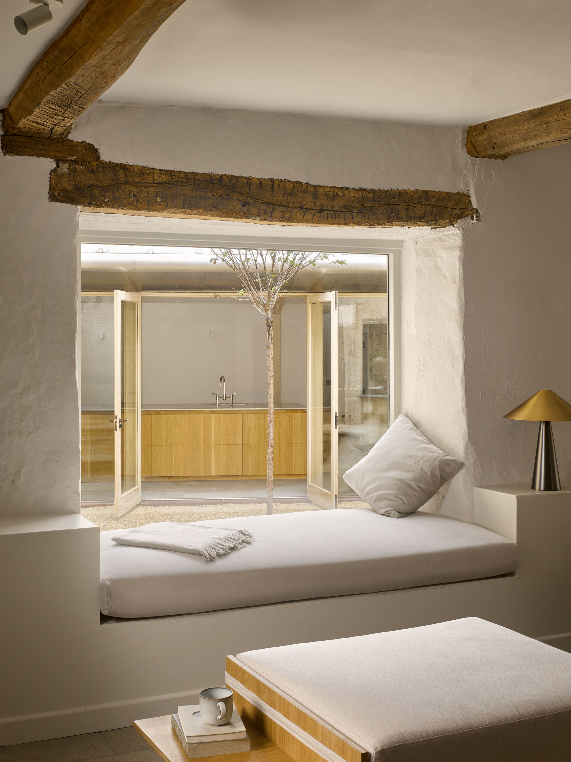 Built-in window seat beneath exposed timber lintel framing a view into the courtyard with a tree