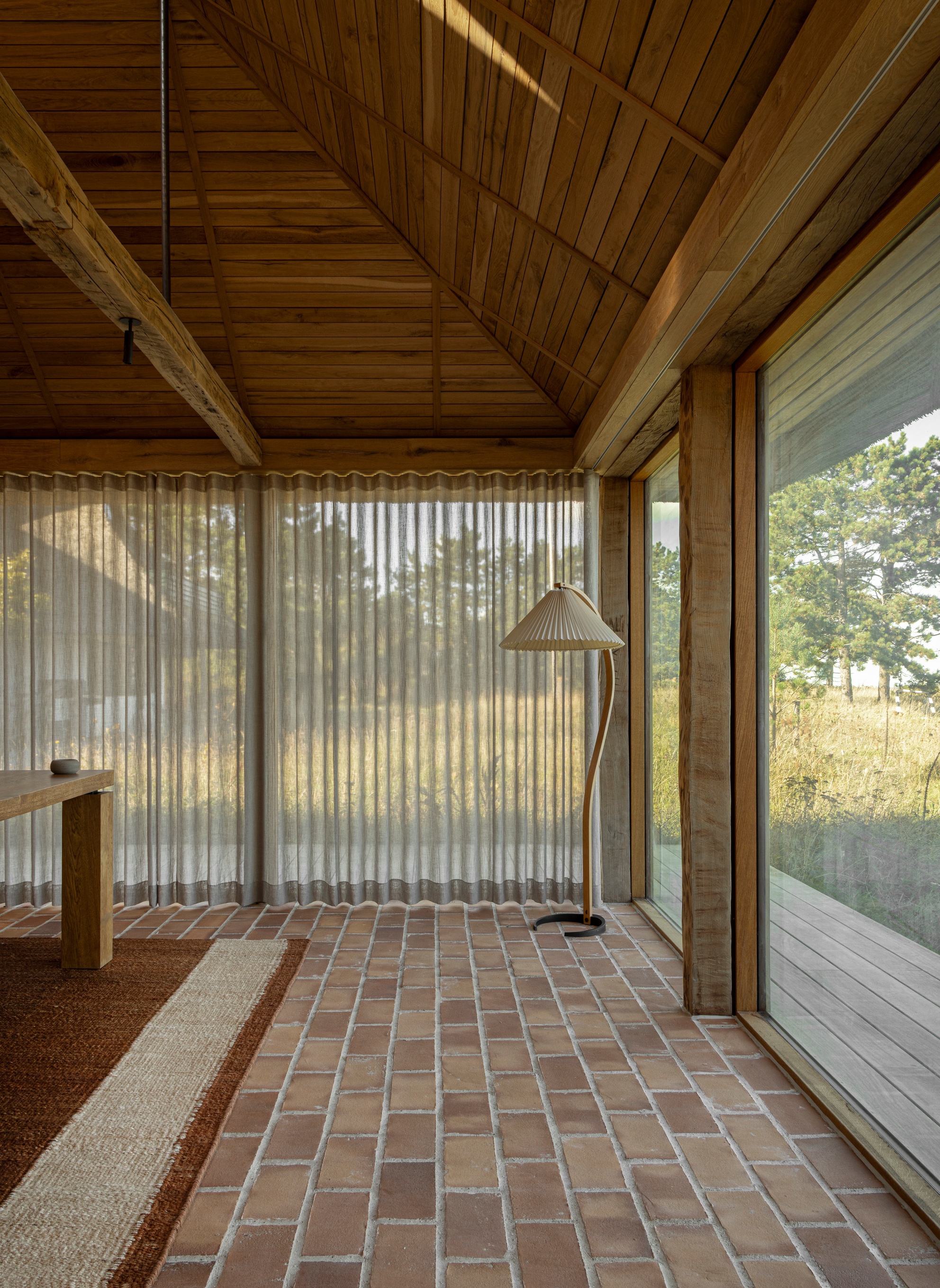 Brick paver floor meeting sheer curtains beneath a pitched timber ceiling in afternoon light
