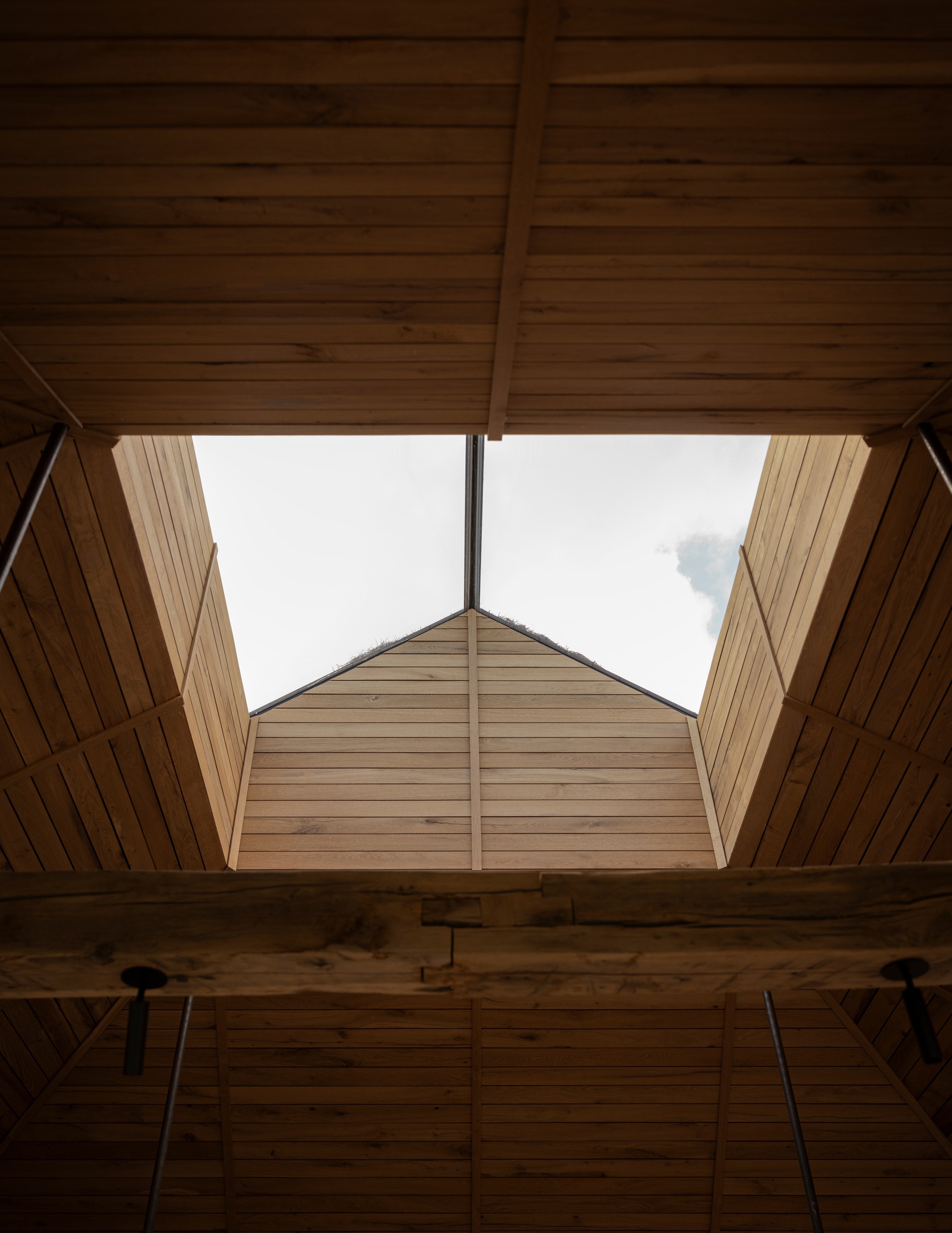 Upward view through a timber-lined skylight opening with exposed beams and pendant light