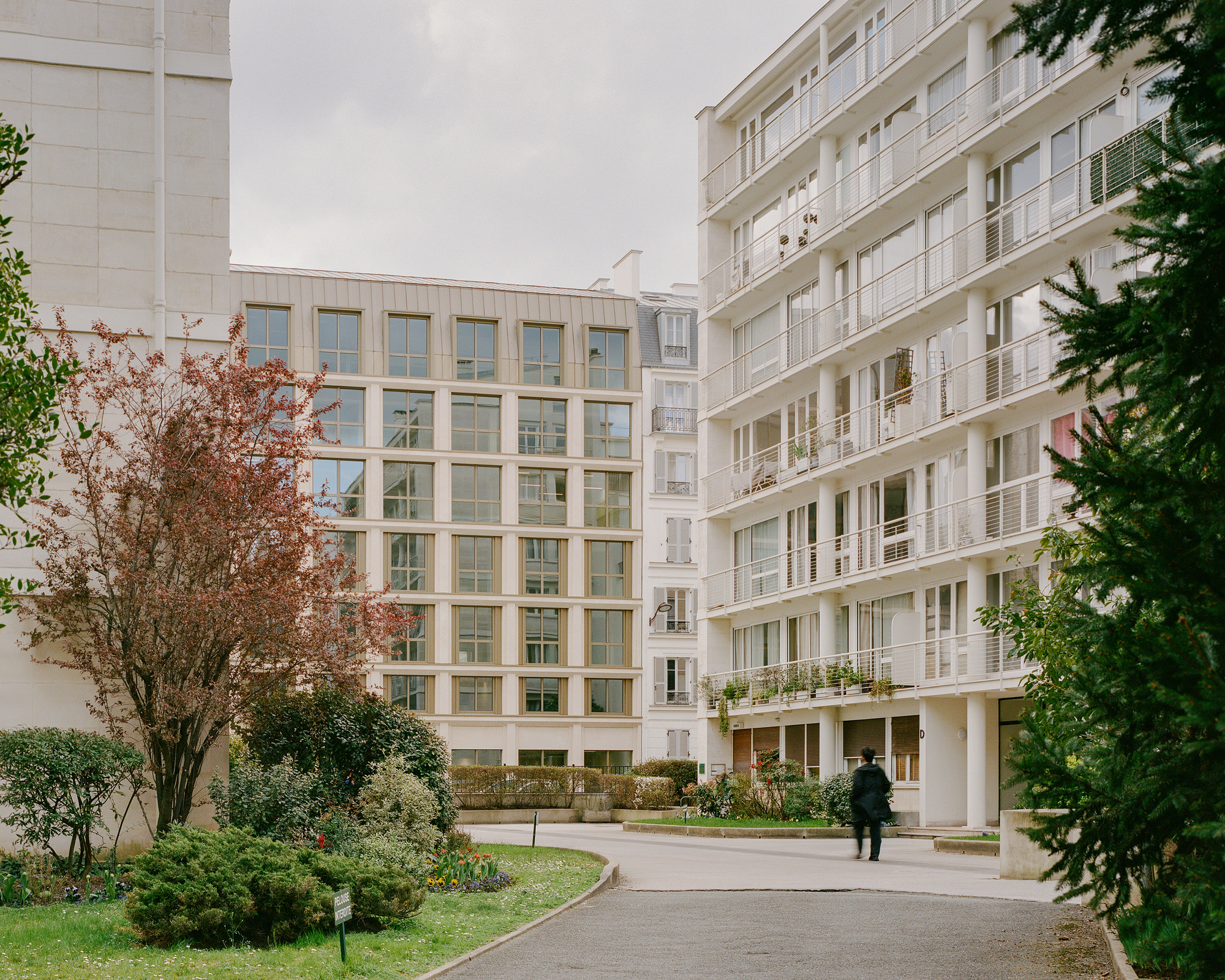 Courtyard view of the window grid facade with a figure walking the curved path in autumn