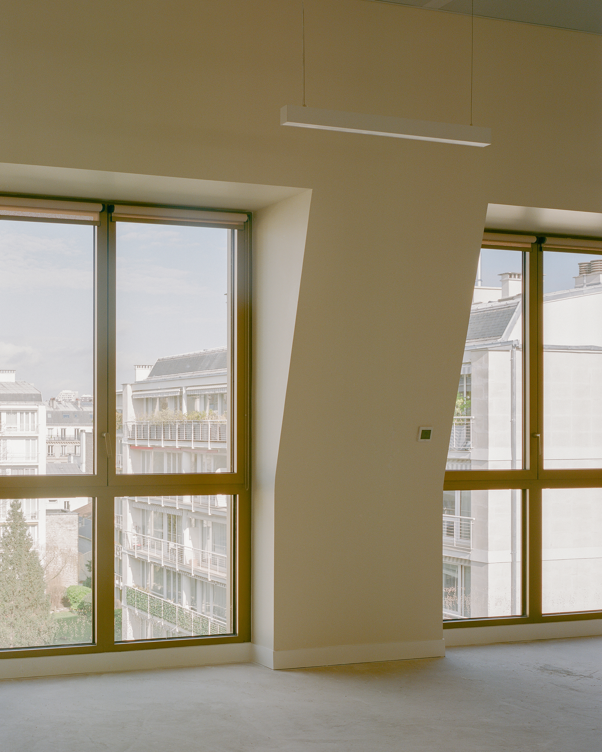 Interior corner with floor-to-ceiling windows framed in bronze metal and a suspended linear light fixture