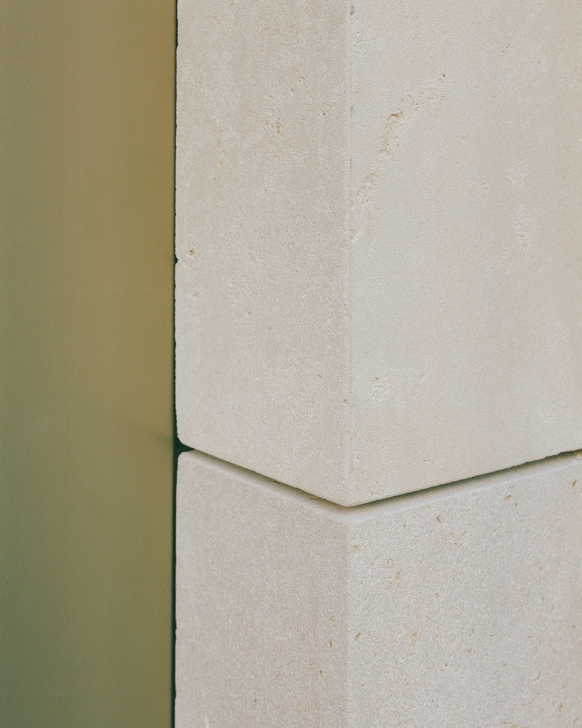 Detail of olive green metal edge meeting a pale stone panel with a chamfered joint