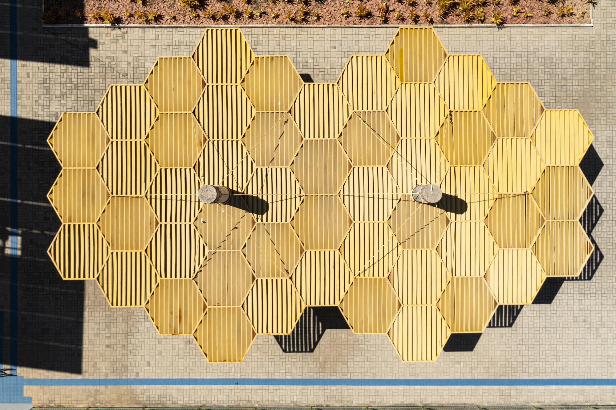 Overhead view of hexagonal yellow canopy modules suspended above open courtyard space