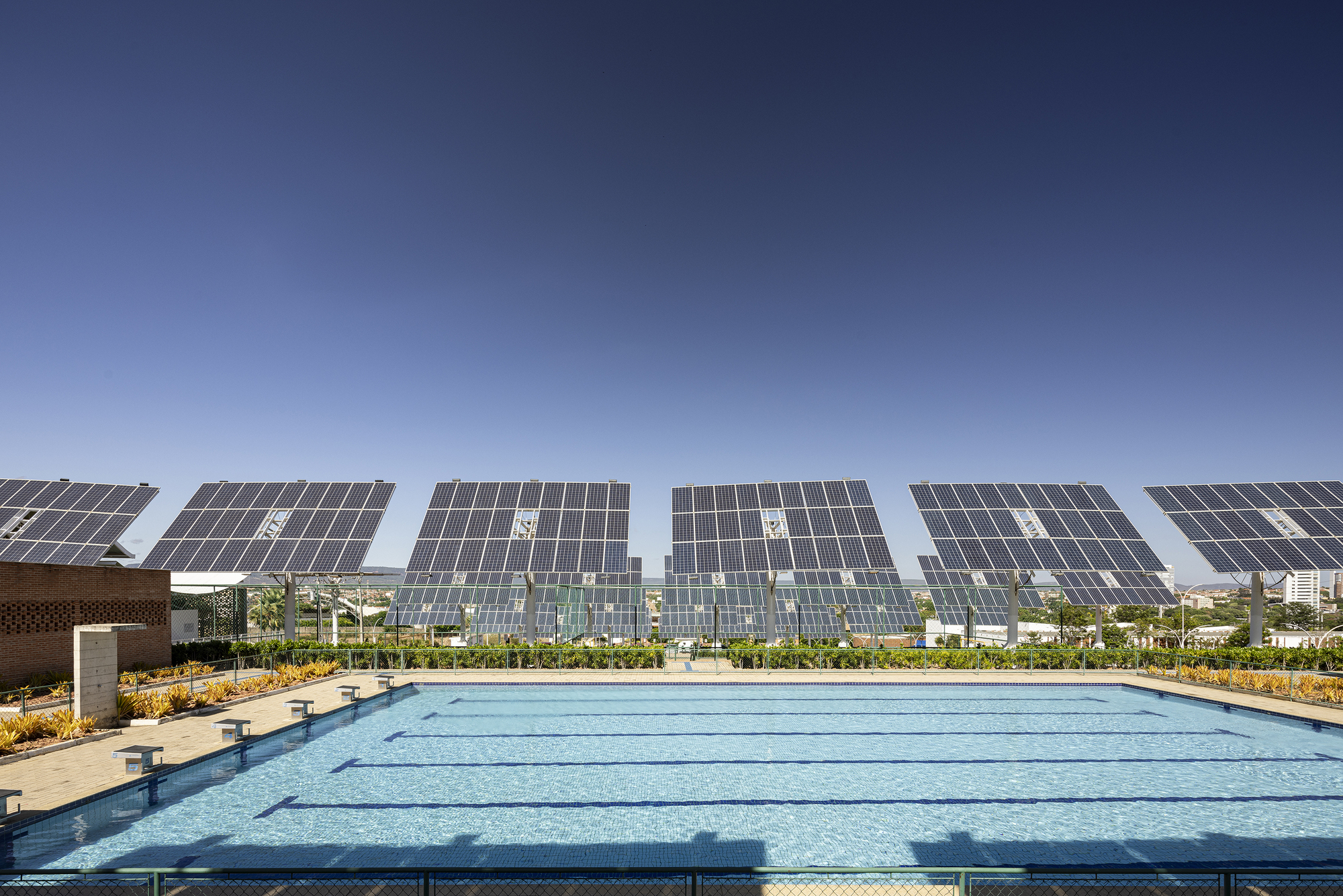 Swimming pool with lane markers beneath array of tilted solar panels and planted beds