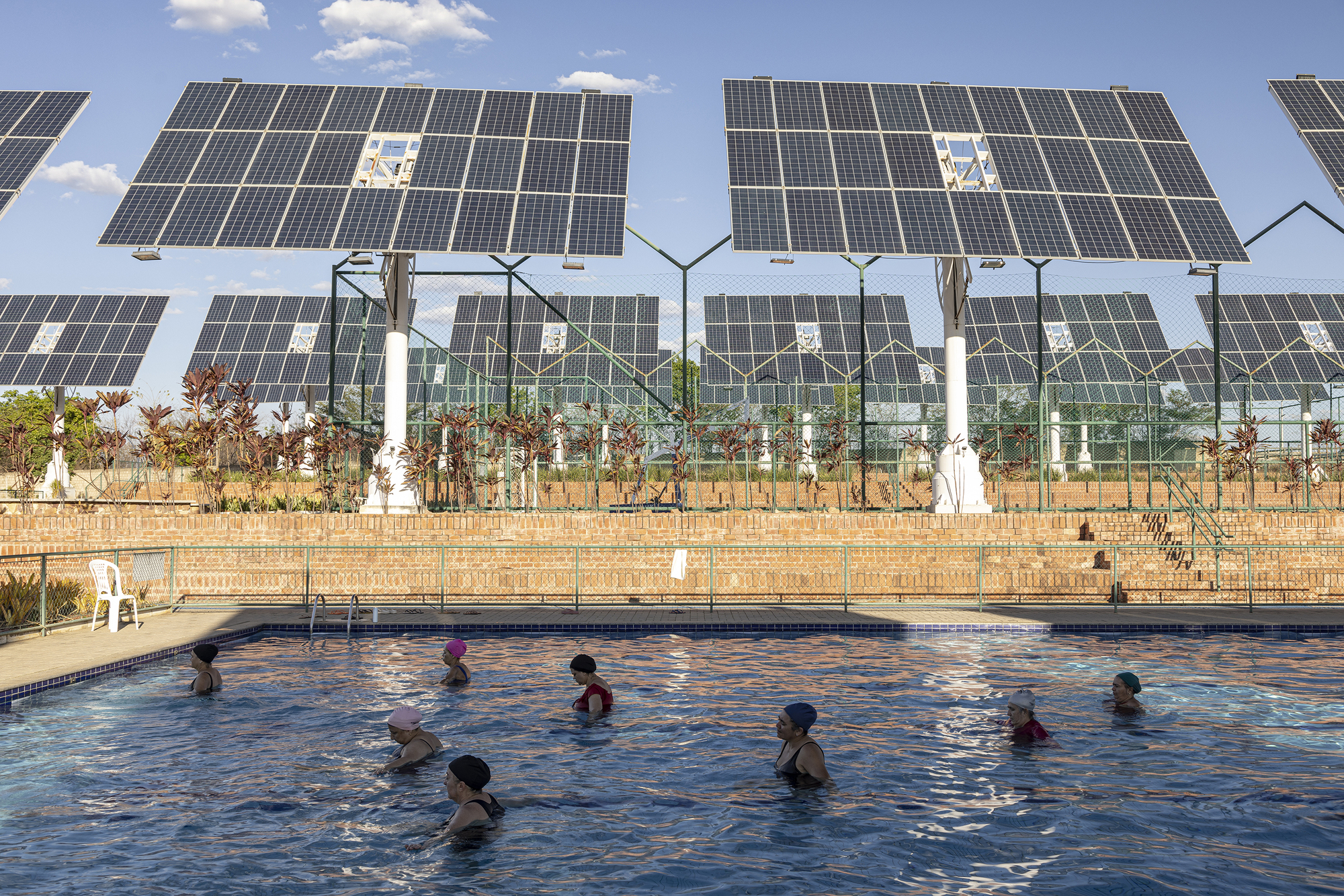 Swimming pool with children in the water backed by tracking solar panels and glass enclosure