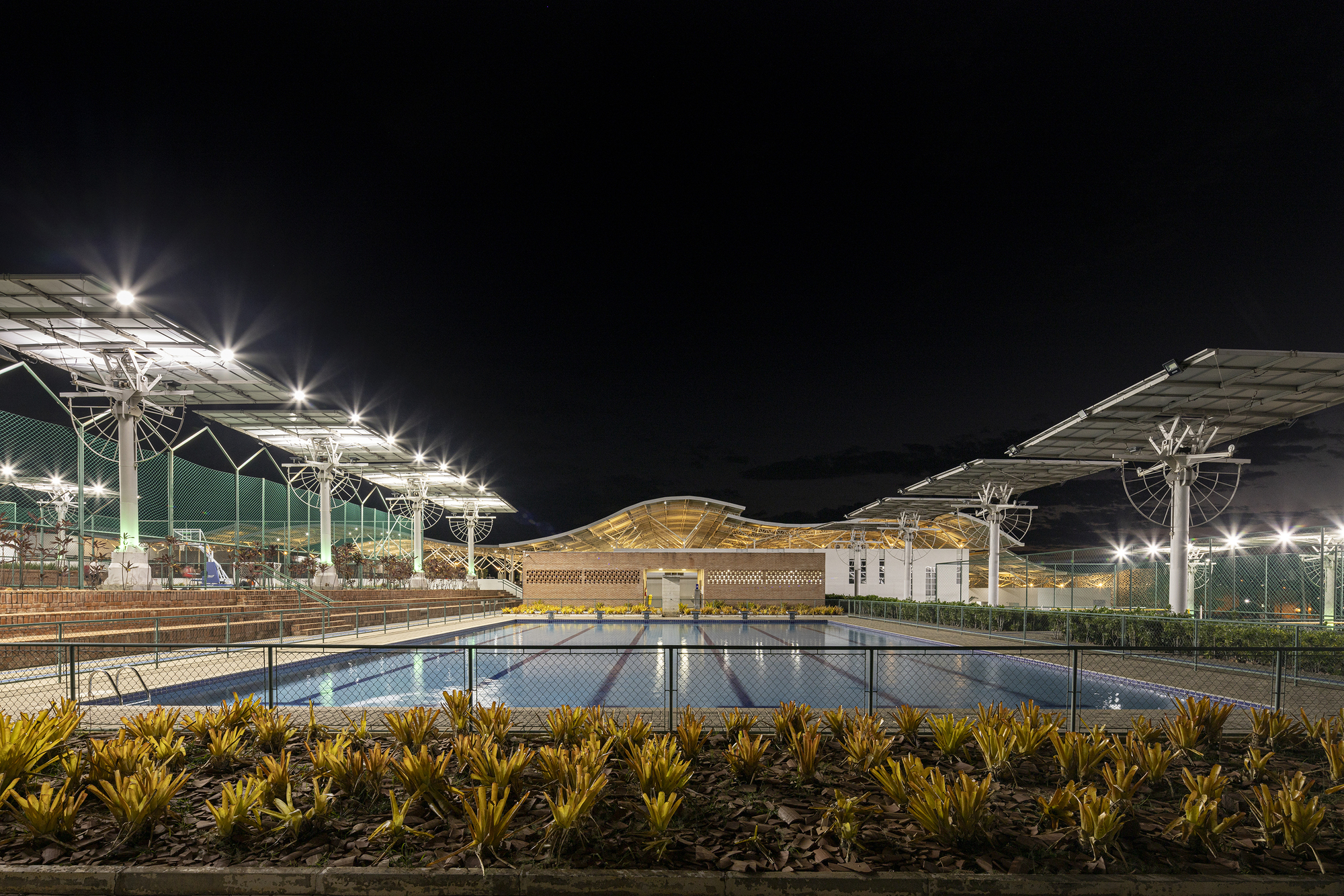 Night view of the reflecting pool with illuminated solar panel canopies and latticed central pavilion