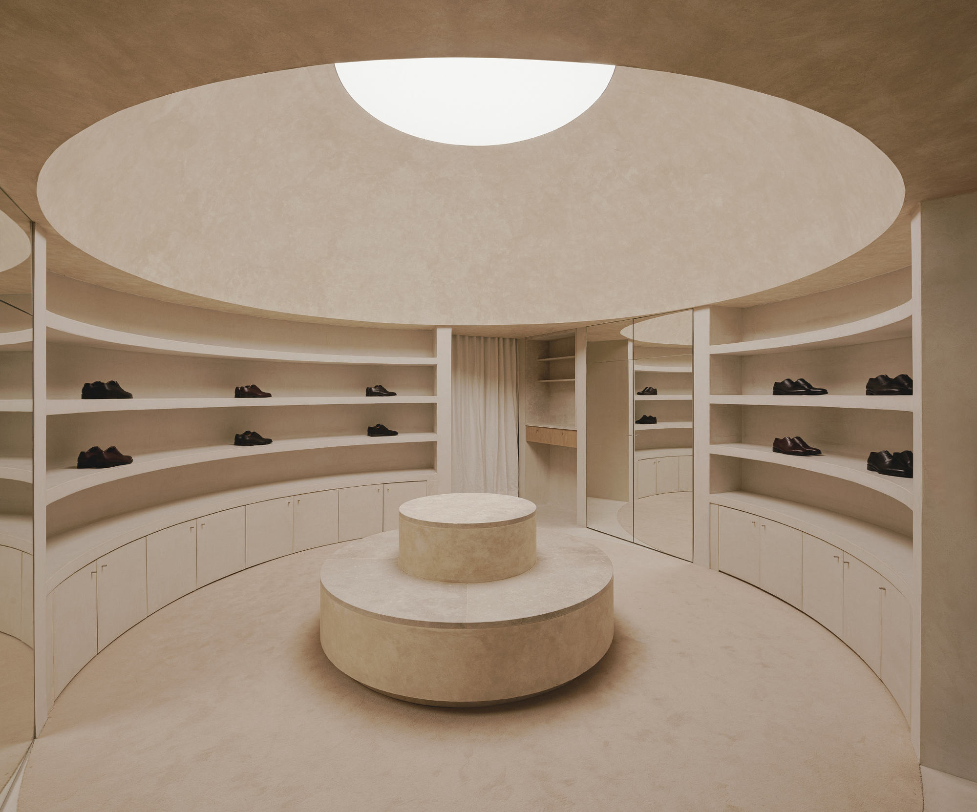 Circular retail interior with curved shelving, tiered central display plinth and circular skylight above
