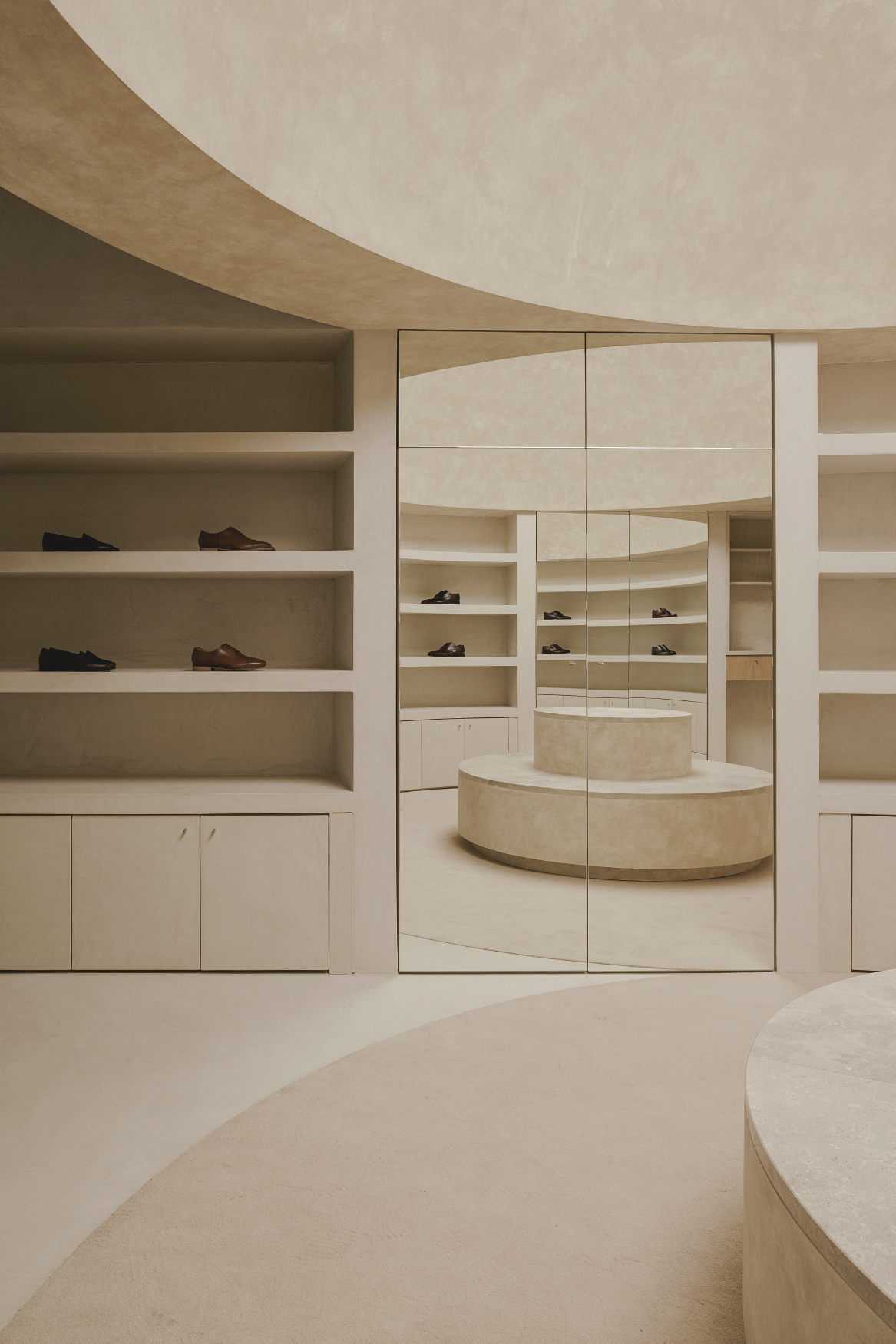 Large mirrored panel reflecting the circular podium and curved display shelves behind
