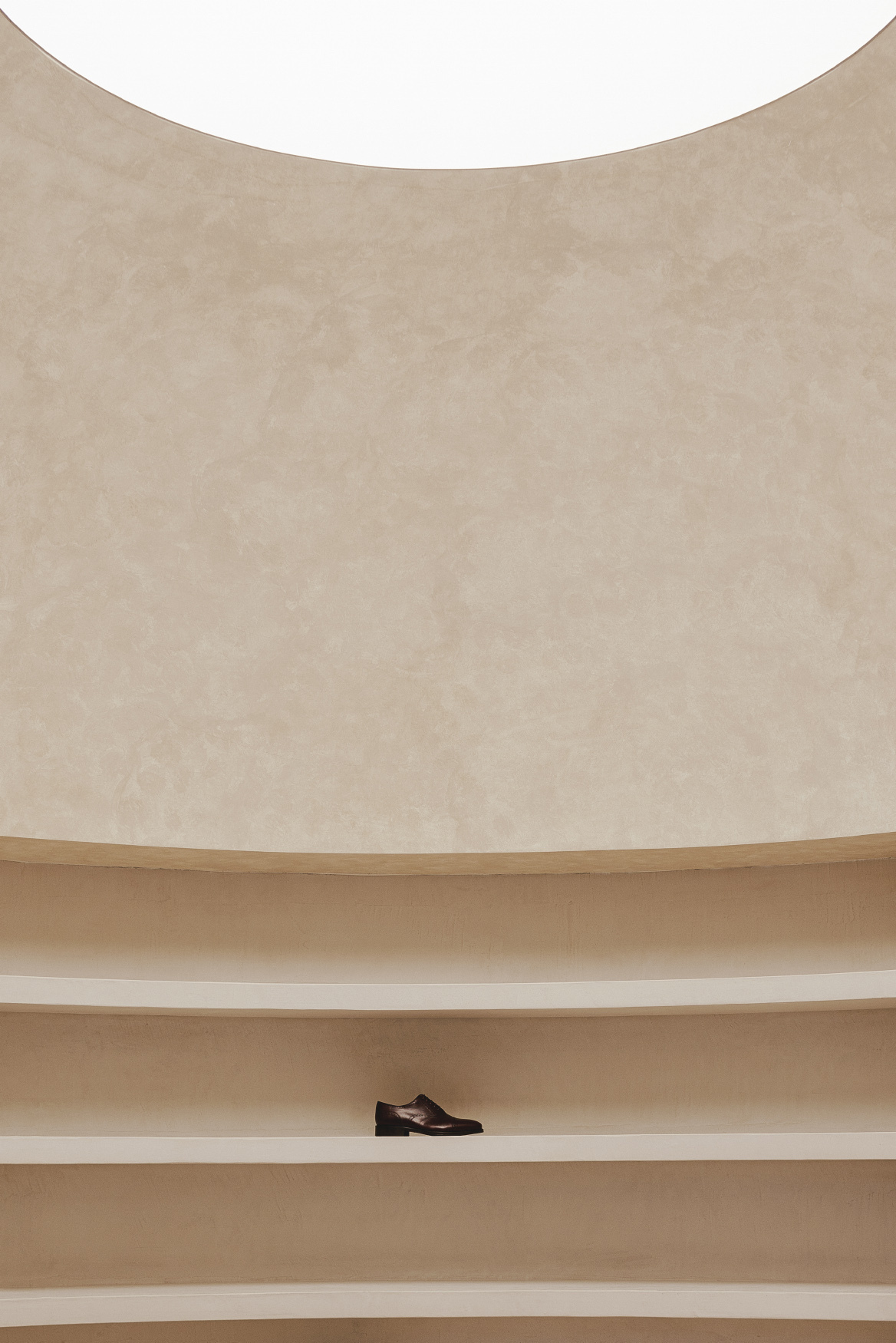 Close-up of curved plaster wall with horizontal timber shelving displaying a single shoe
