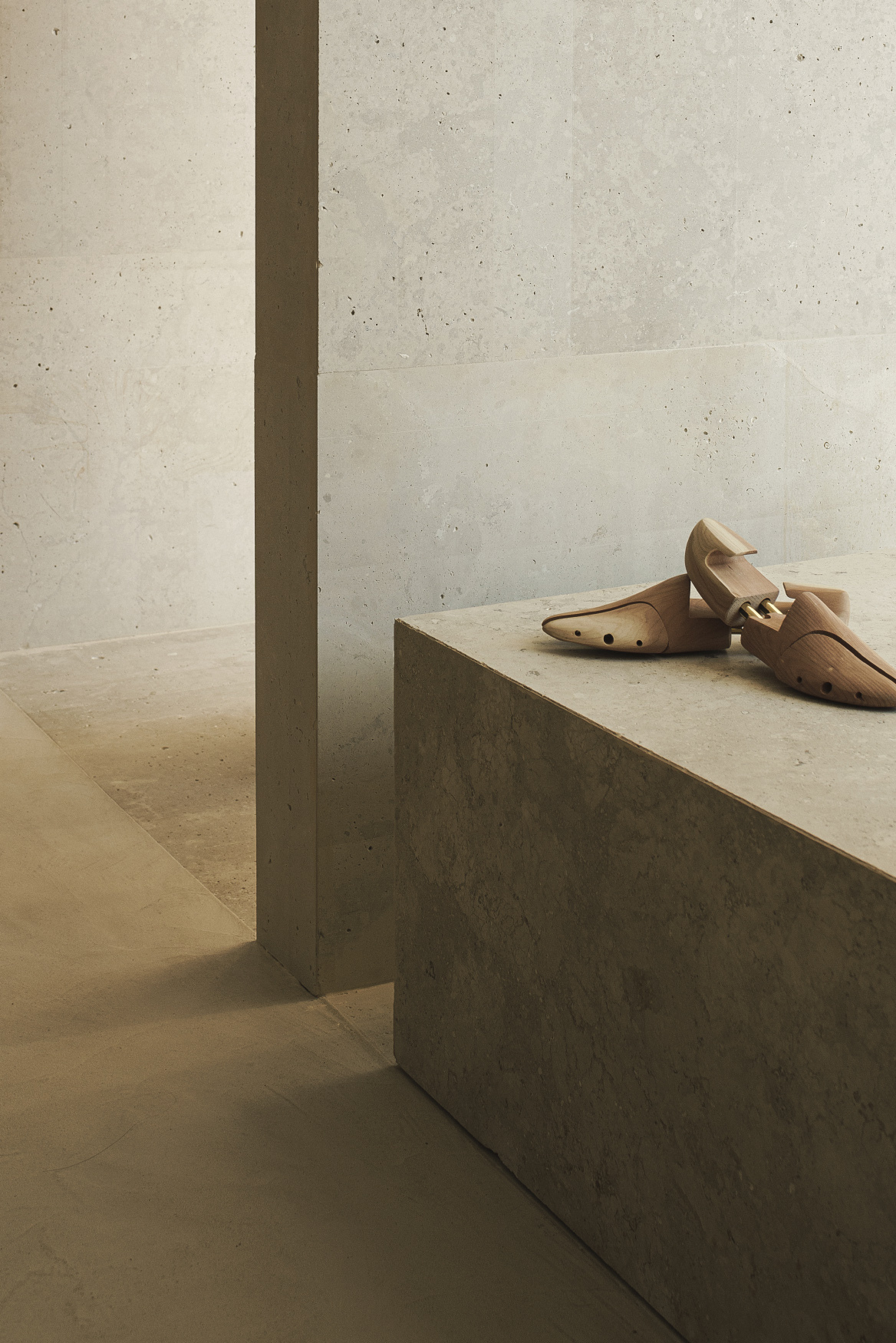 Concrete display plinth beside recessed pilaster against board-formed concrete wall under natural light
