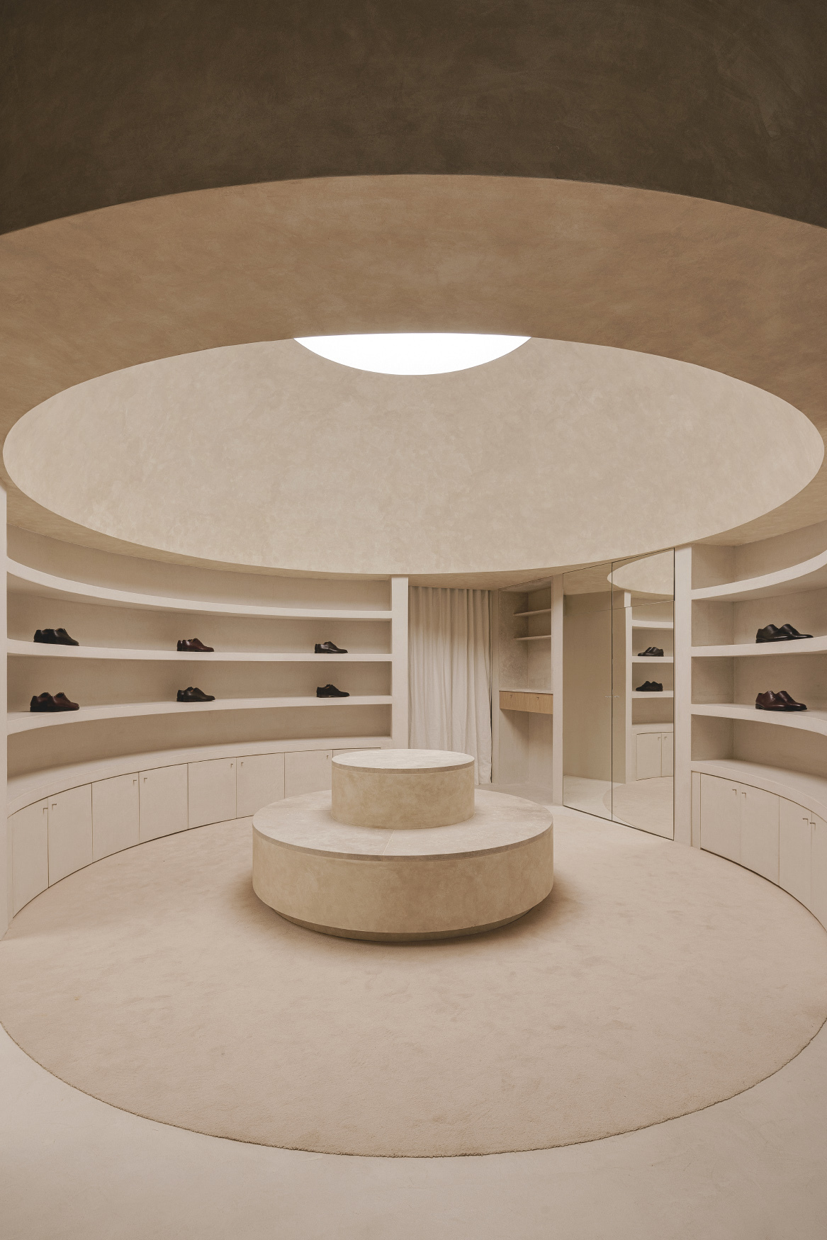 Circular retail space with tiered sandstone ceiling, central oculus, and curved display shelving around a cylindrical plinth
