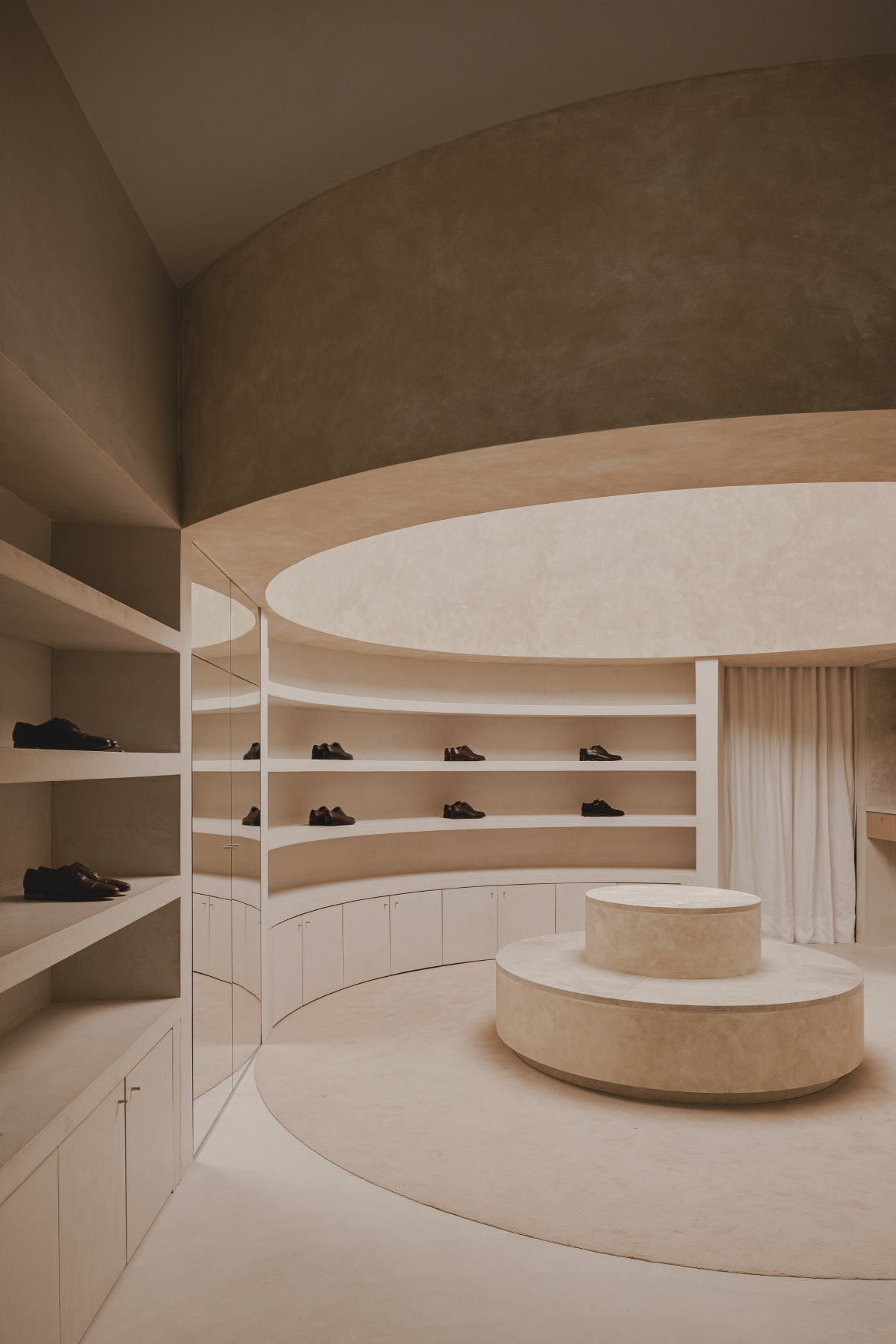 Curved display shelving with shoes set into continuous horizontal niches below layered ceiling bands