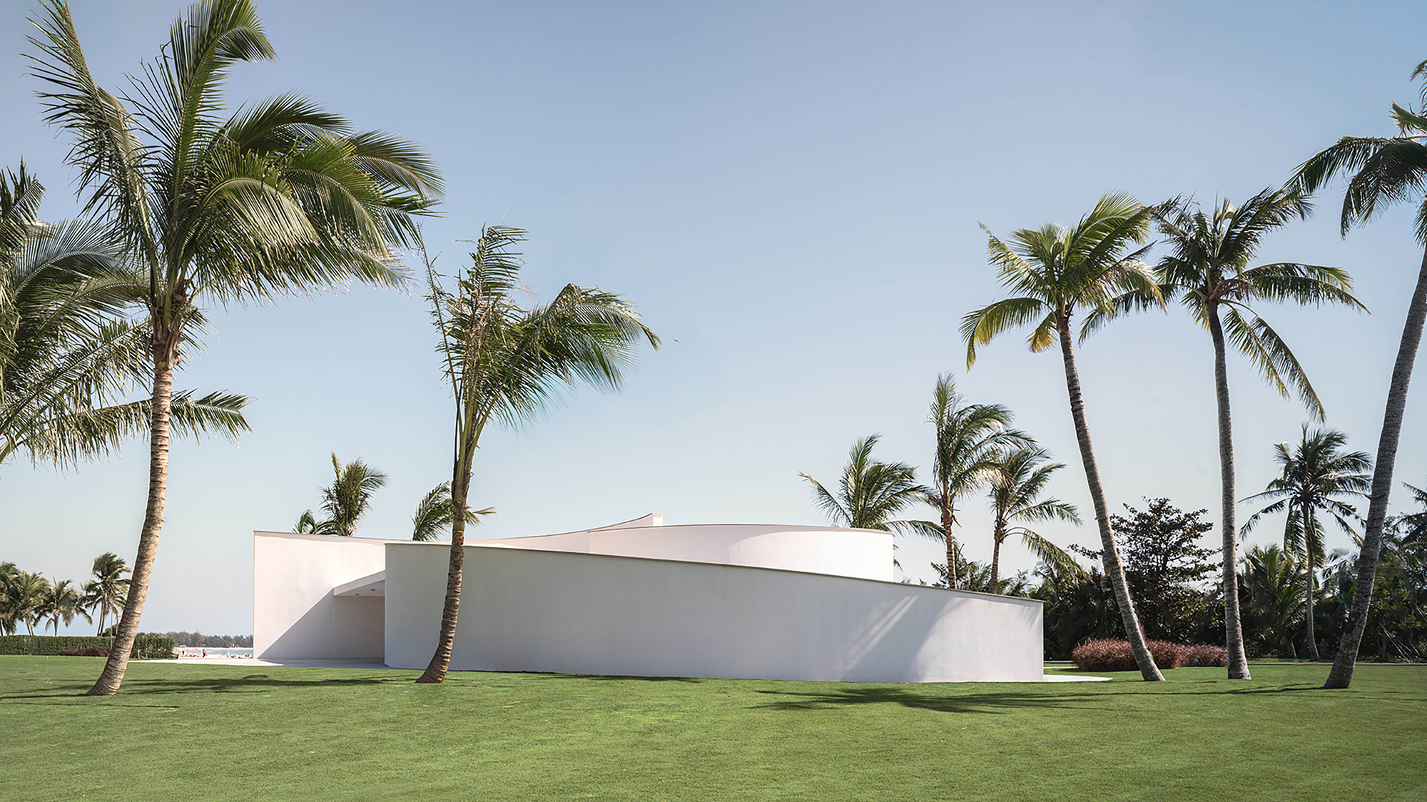 Side elevation of the curved white volume with arched opening beneath swaying palm trees