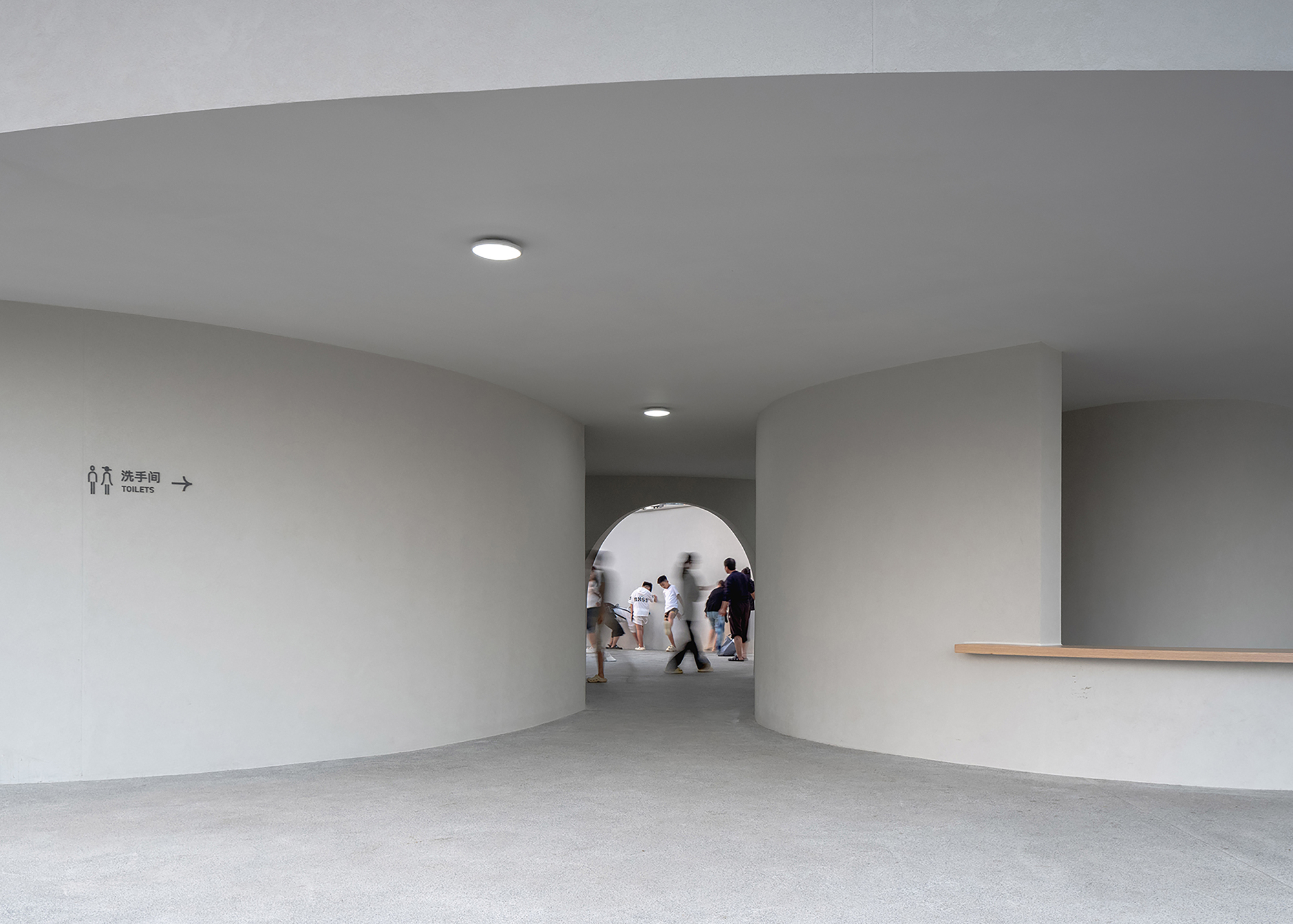 Interior corridor with circular opening and visitors walking through under recessed ceiling lighting