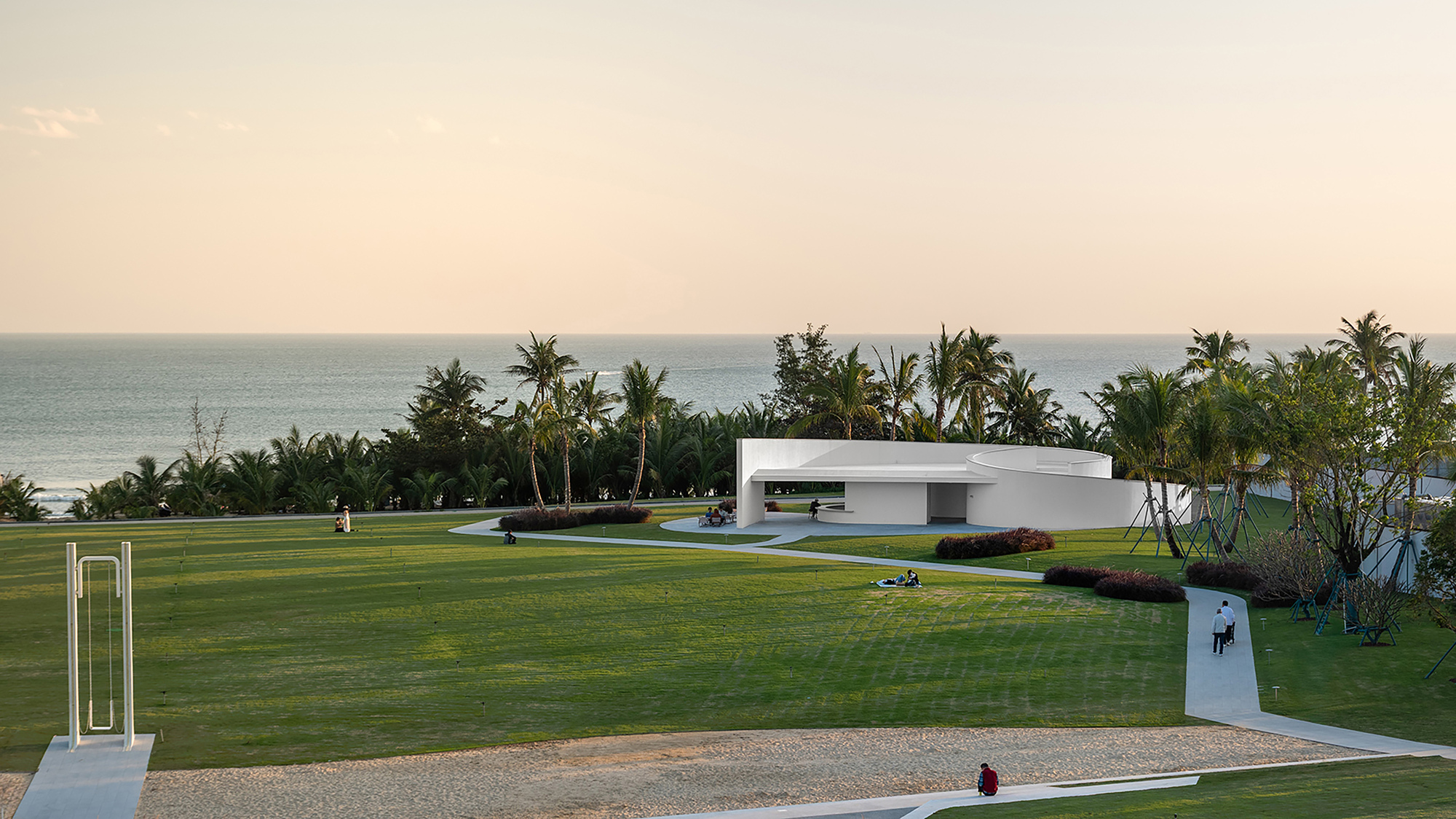 Low horizontal volume with recessed openings set in a mowed lawn facing the ocean at sunset