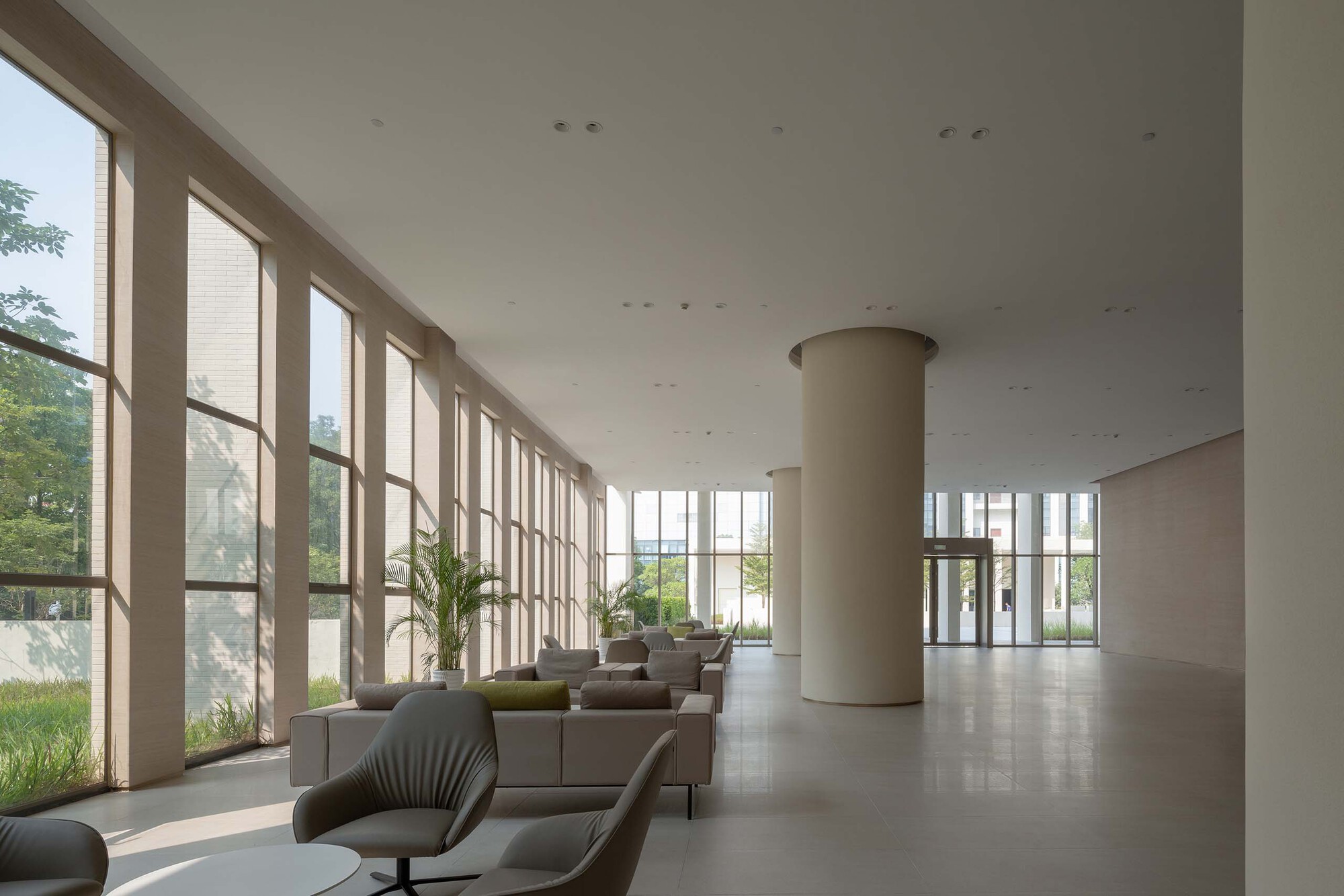 Lobby interior with tall floor-to-ceiling windows, cylindrical column and scattered lounge seating under soft daylight