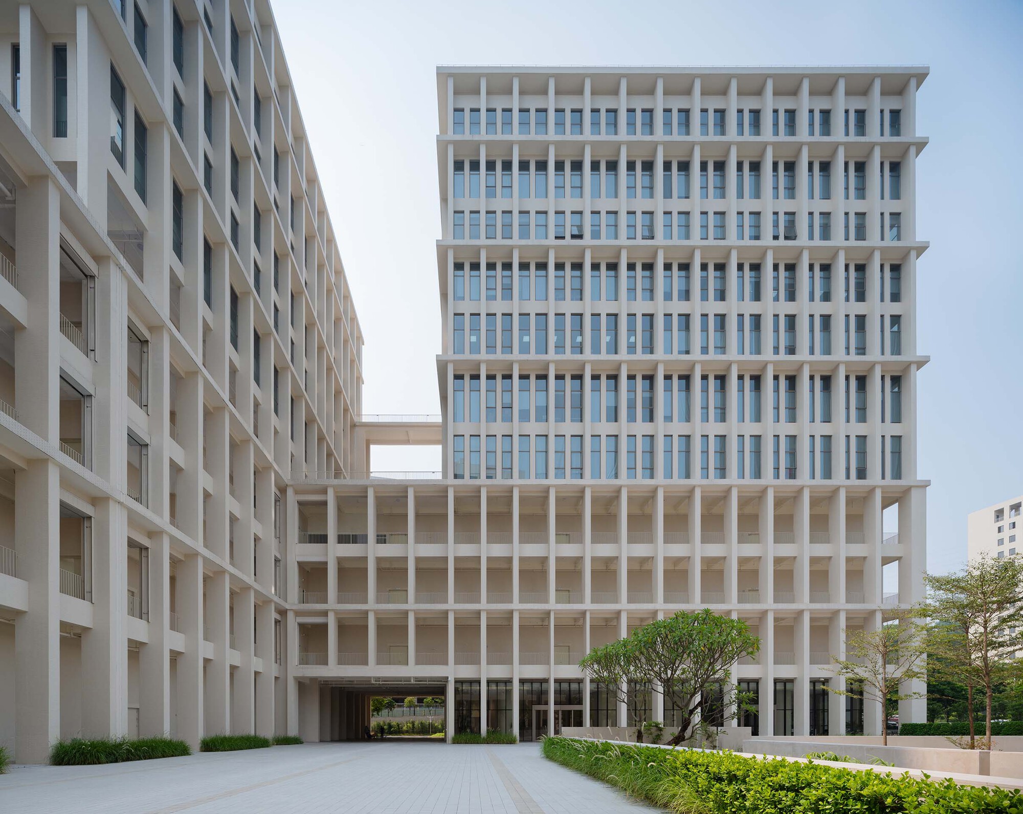 Courtyard view between two gridded tower blocks connected by a central elevated walkway