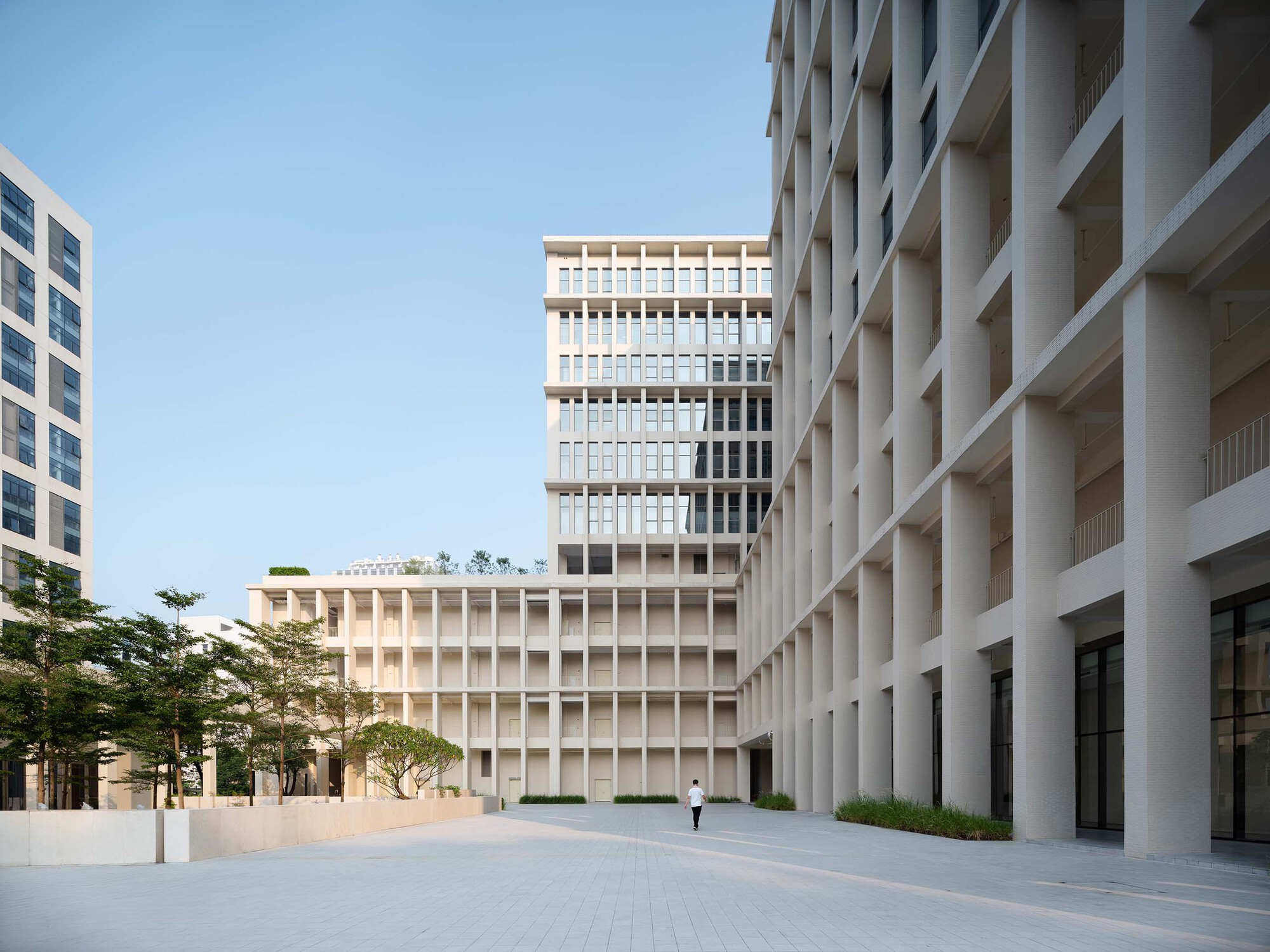 Plaza framed by precast concrete facades with deep vertical fins and a lone pedestrian