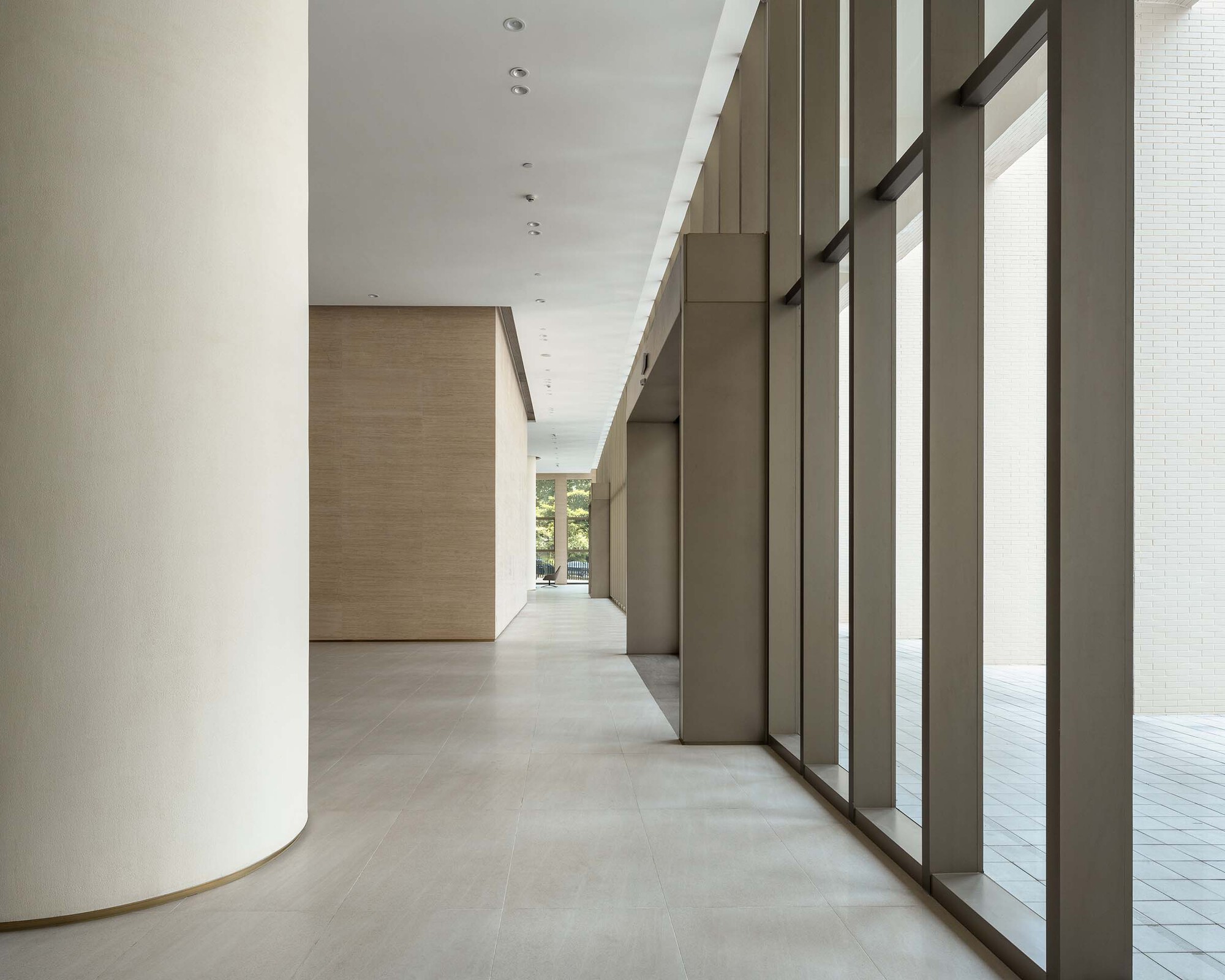 Lobby corridor with curved white column, bronze metal screens and pale stone flooring