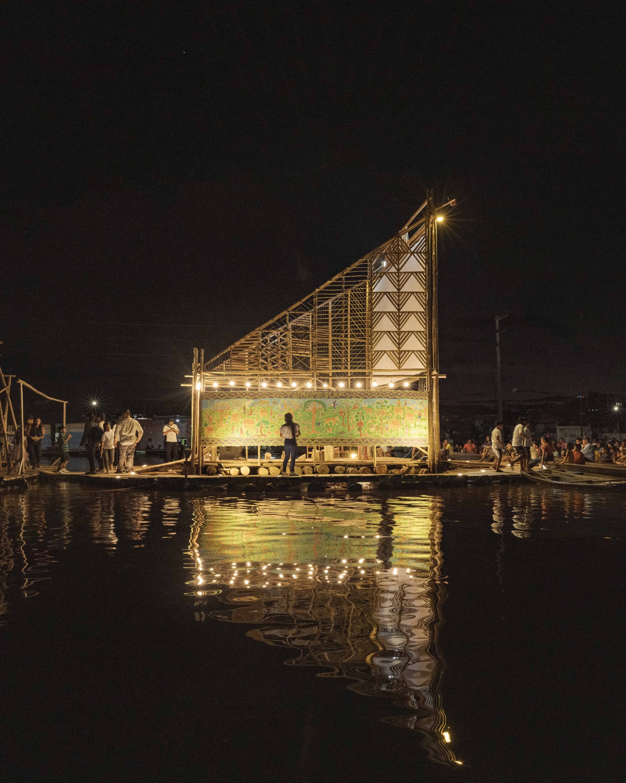 Floating platform with angled bamboo frame and glowing screen reflected in calm water at night