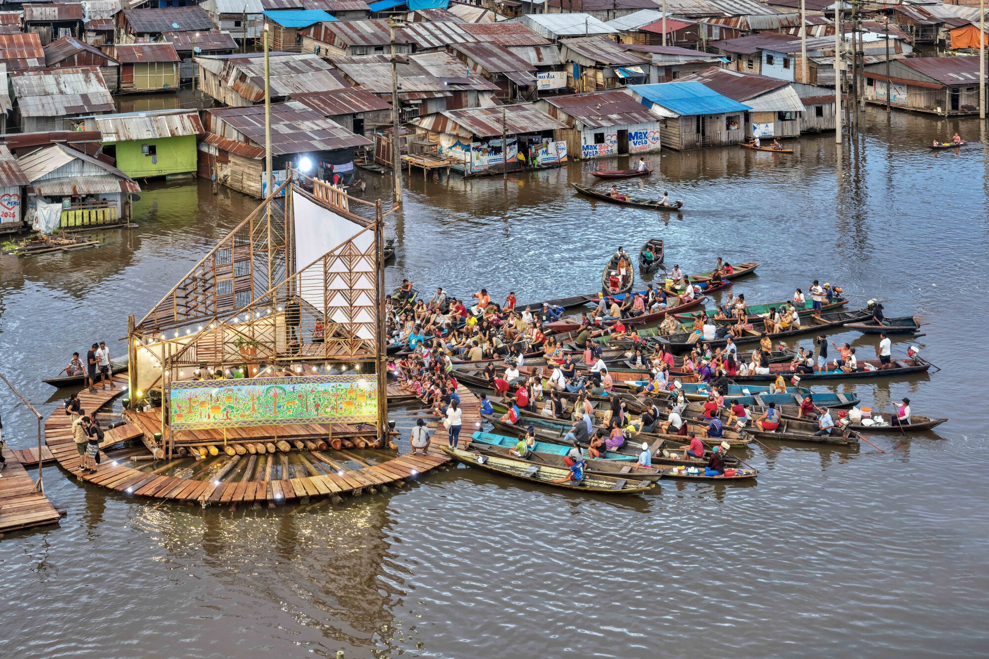 Floating timber platform stage surrounded by dozens of canoes gathering in the water