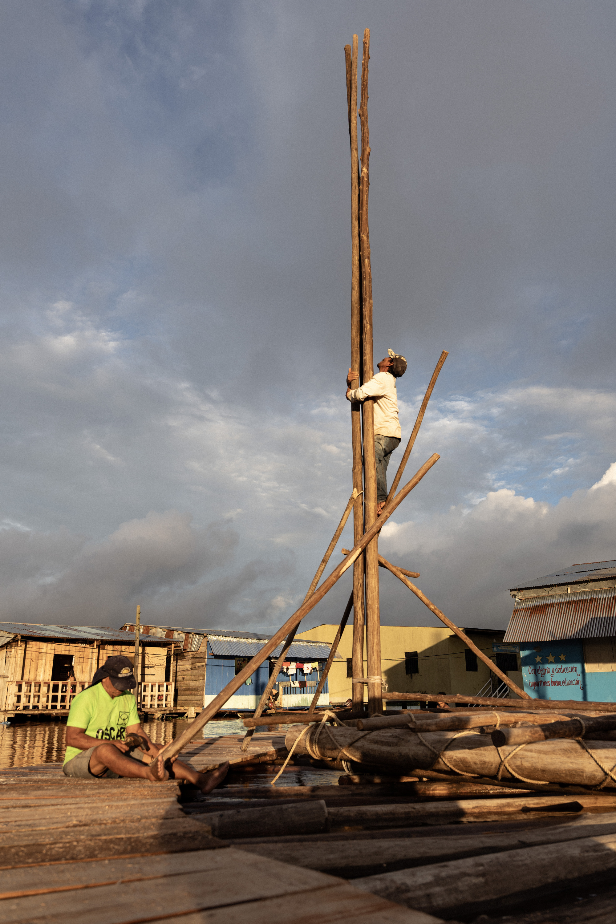 Timber tripod structure being erected on a floating bamboo platform at golden hour