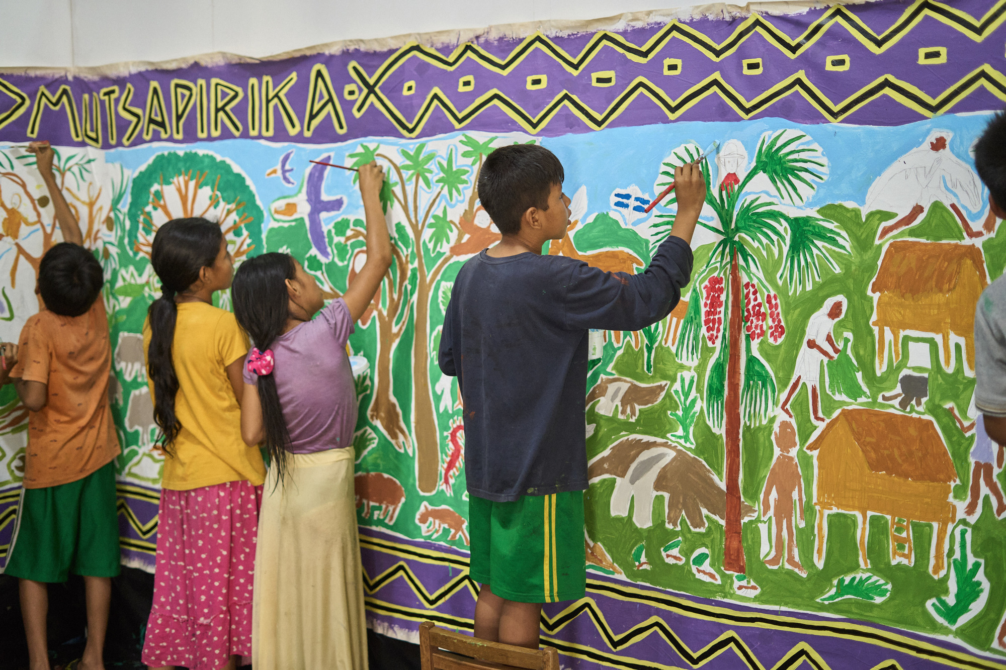 Children painting a mural depicting tropical vegetation and animals on an interior wall panel