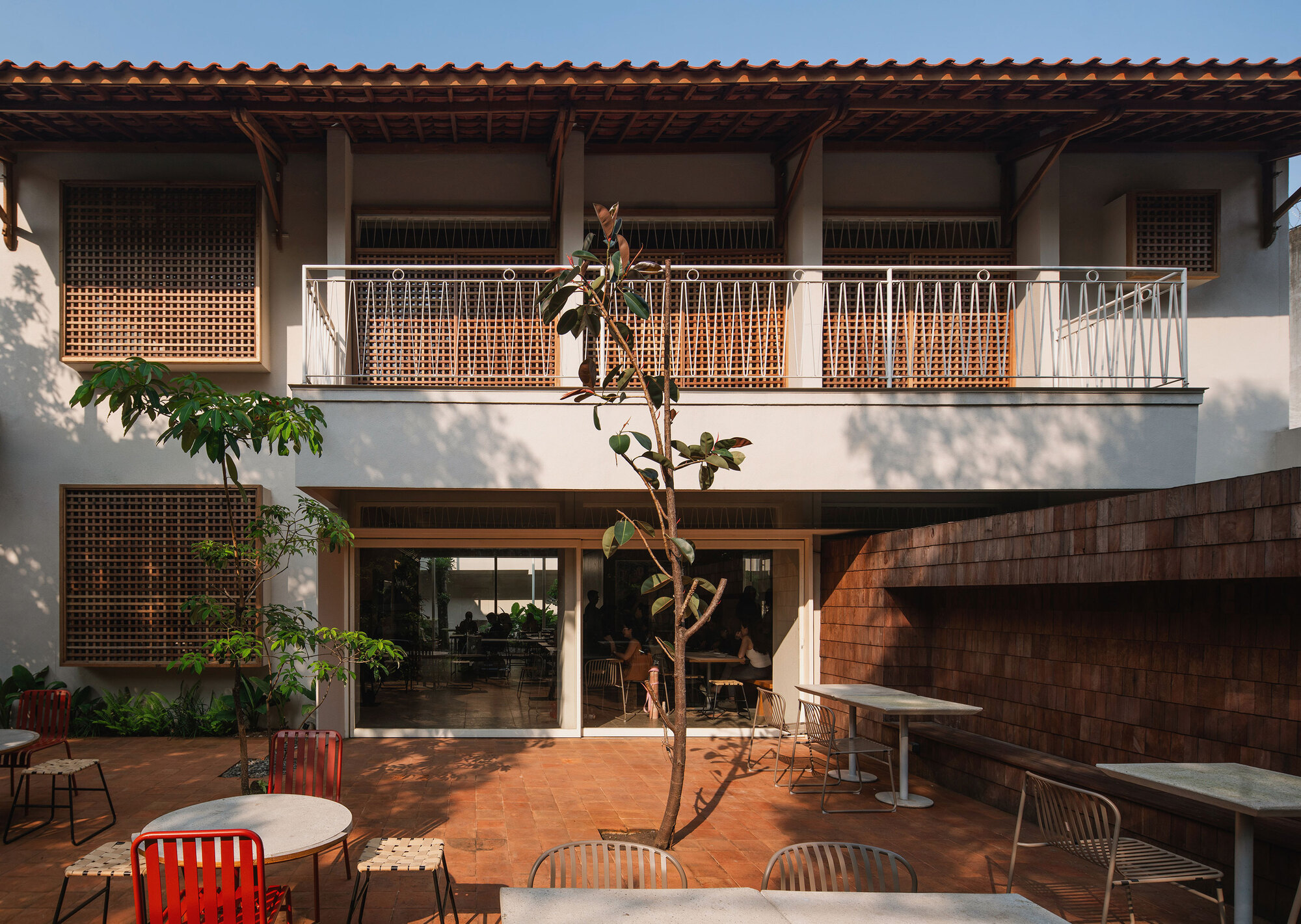 Interior courtyard with terracotta paving, lattice screens and a white metal balcony rail under afternoon sun