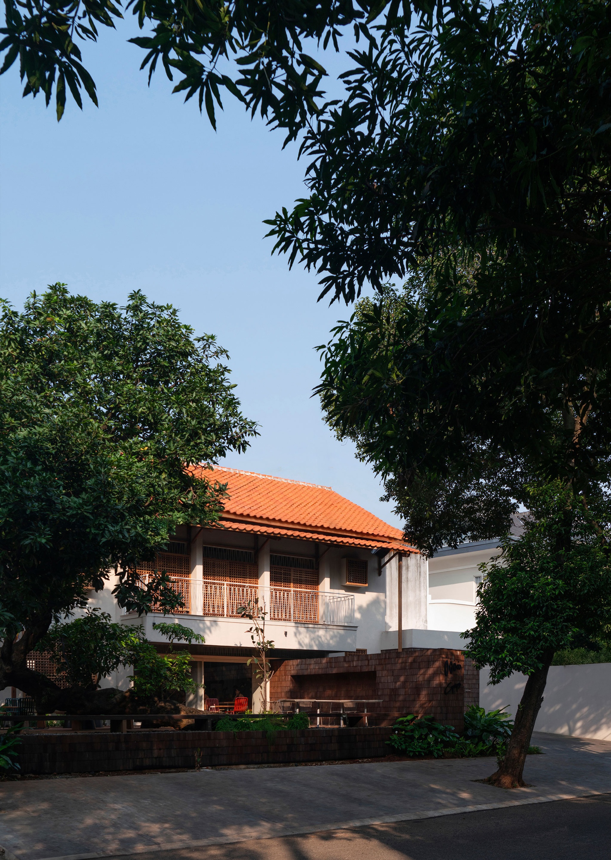 Two-storey facade with orange clay tile roof framed by overhanging tree canopy at dusk
