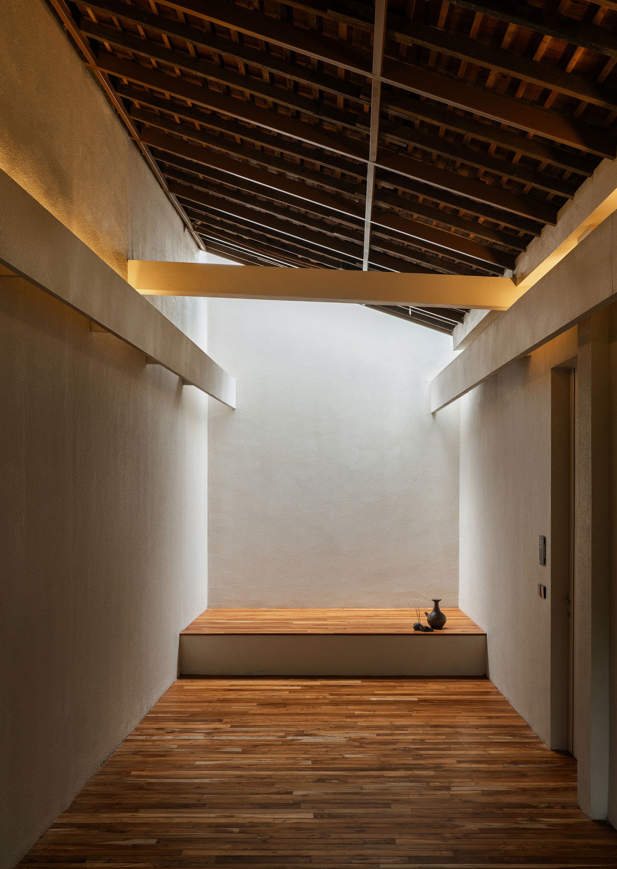 Timber hallway with exposed rafter ceiling and white plaster walls leading to an elevated seating platform