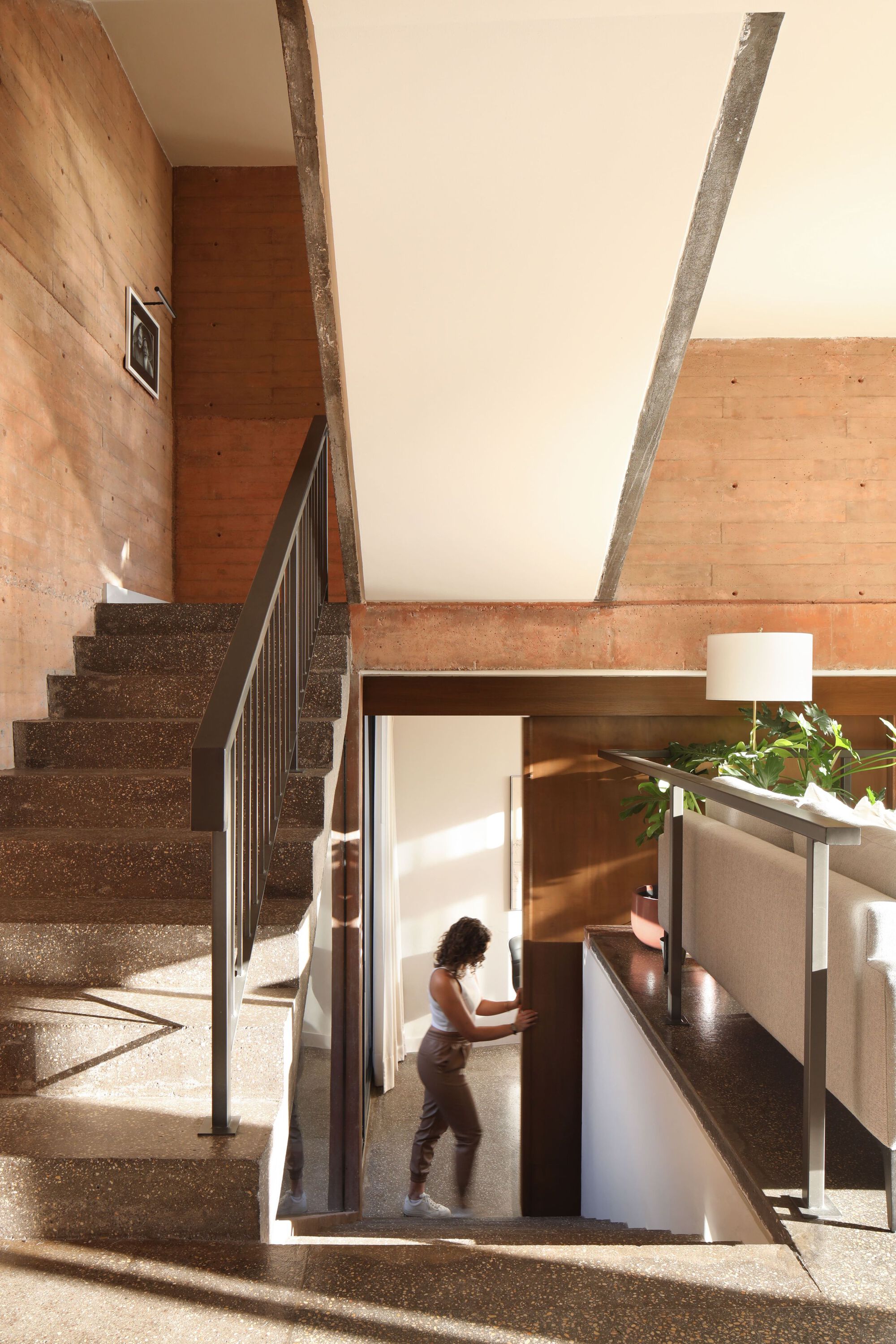 Interior stairwell with exposed concrete beams and figure descending through sunlit opening