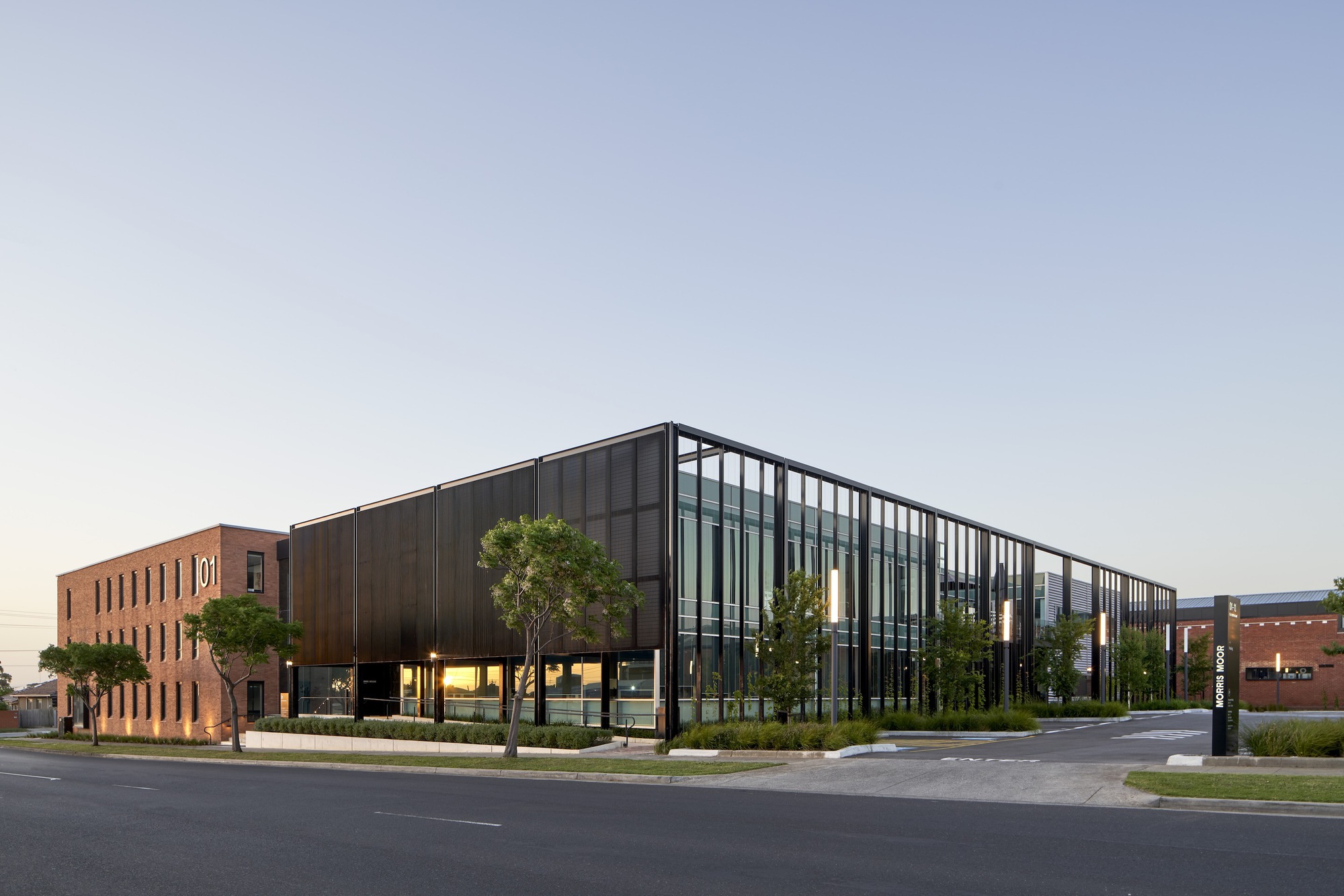 Street corner view of the dark perforated metal facade and glass curtain wall at dusk
