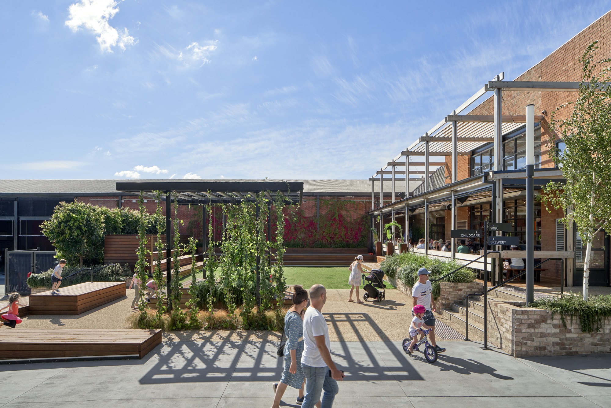 Elevated view of the courtyard with planted trellis structure and families moving through sunlit pathways