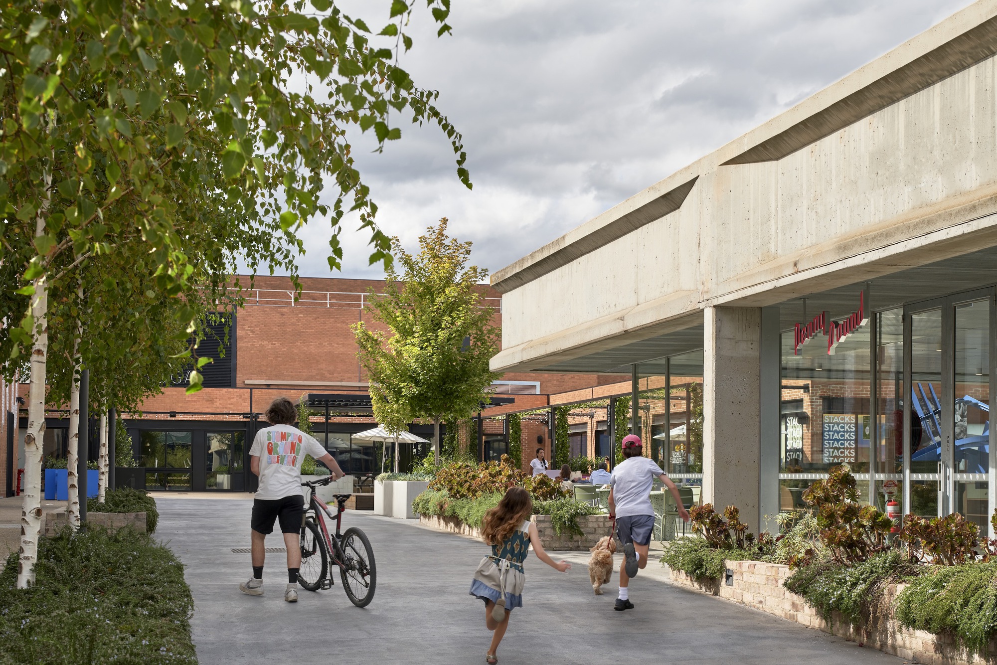 View along the concrete canopy edge with shopfront glazing and families walking under overcast skies