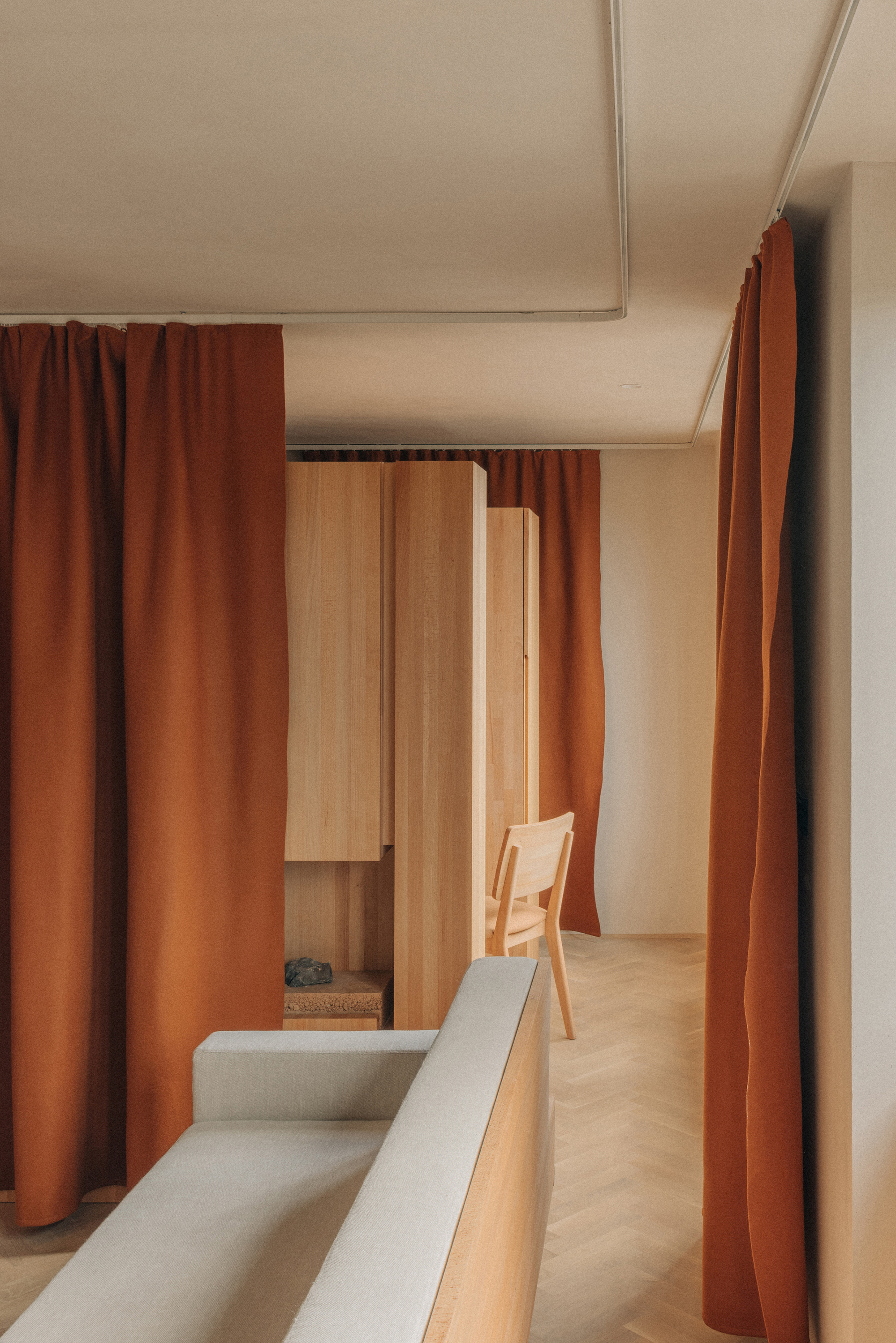 Upholstered bench along corridor framed by timber cabinetry and suspended ceiling panels