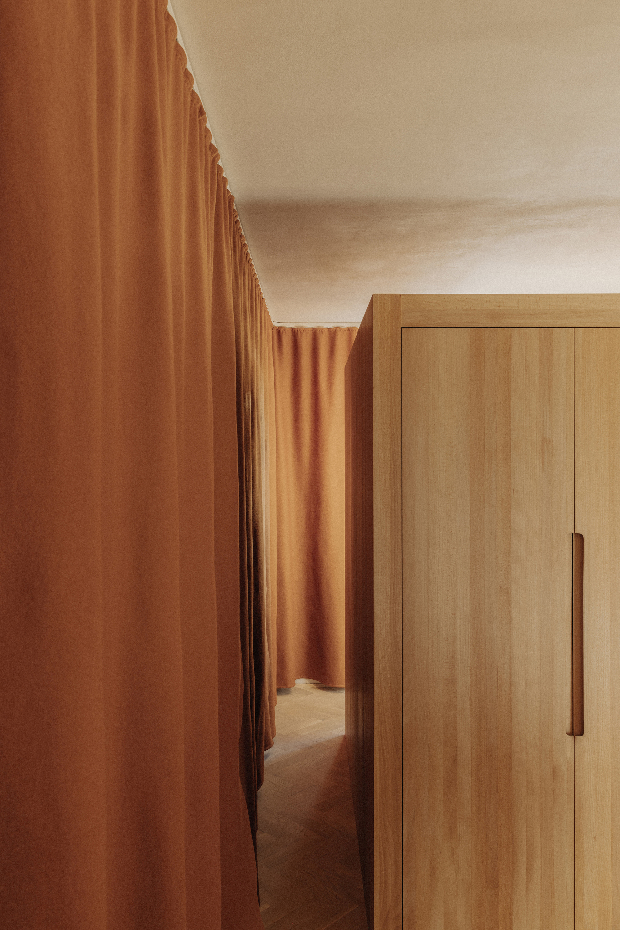 Narrow passage between terracotta fabric and timber wardrobe with vertical pull handle