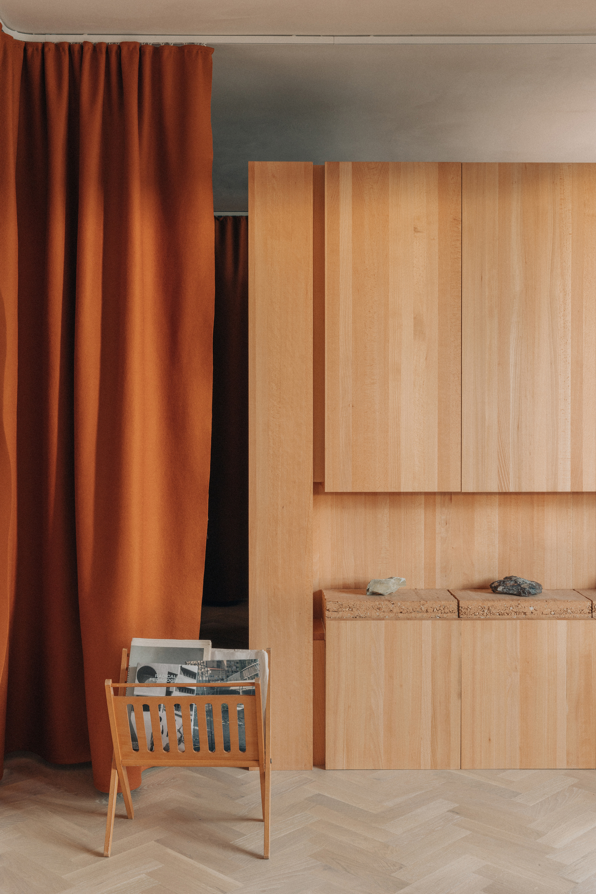 Light timber cabinetry with cork shelf recess beside terracotta curtains and timber magazine holder