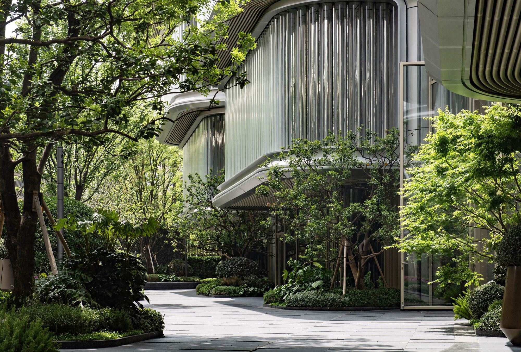Curved louvered facade nestled among mature trees with ground-level planted beds