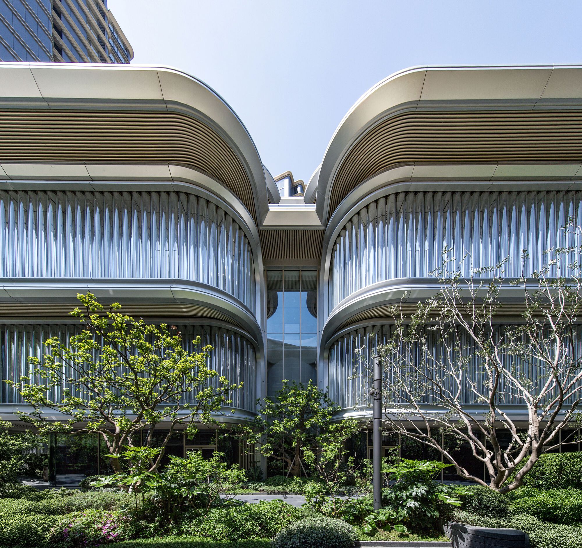 Symmetrical curved facade volumes with vertical fins and bronze louvers viewed from the landscape
