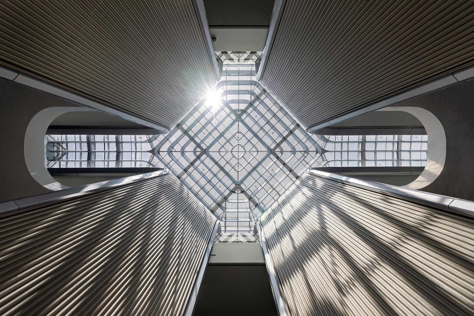 Looking up at diamond-shaped skylight framed by ribbed ceiling panels and curved balcony edges