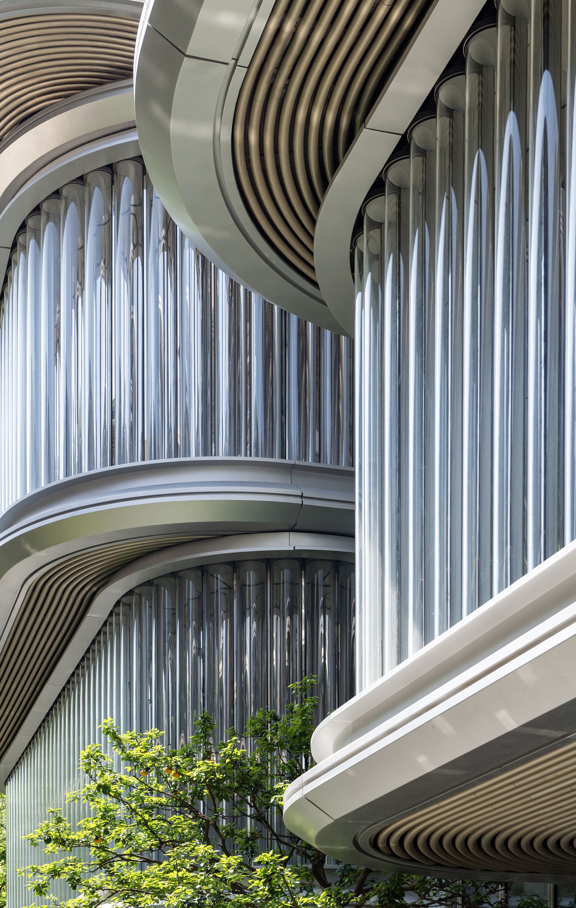 Curved balconies with vertical metal slats and ribbed soffits wrapping around planted greenery