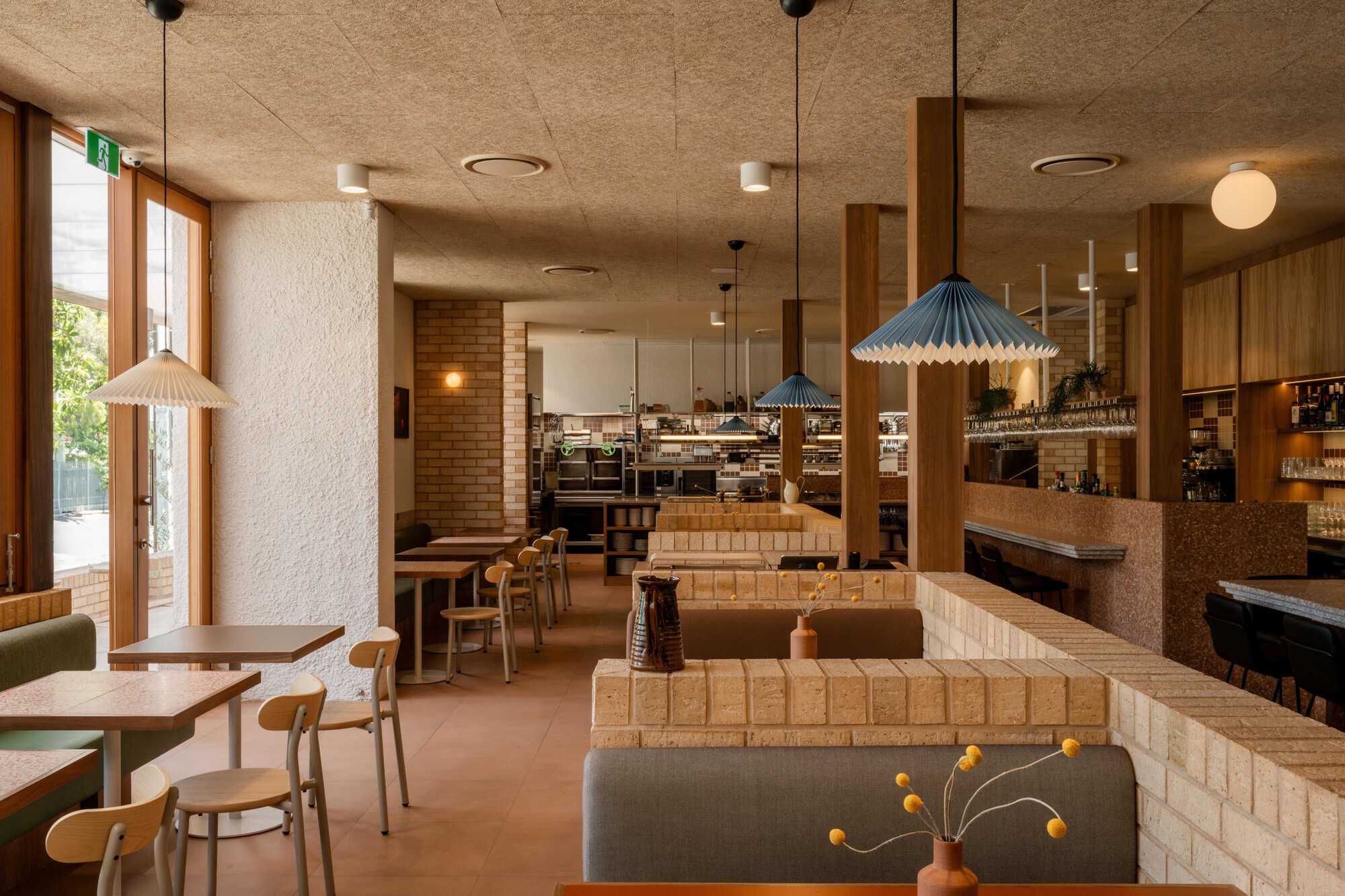 Open dining room showing cream tile partitions, pendant lights, and timber joinery under a textured concrete soffit