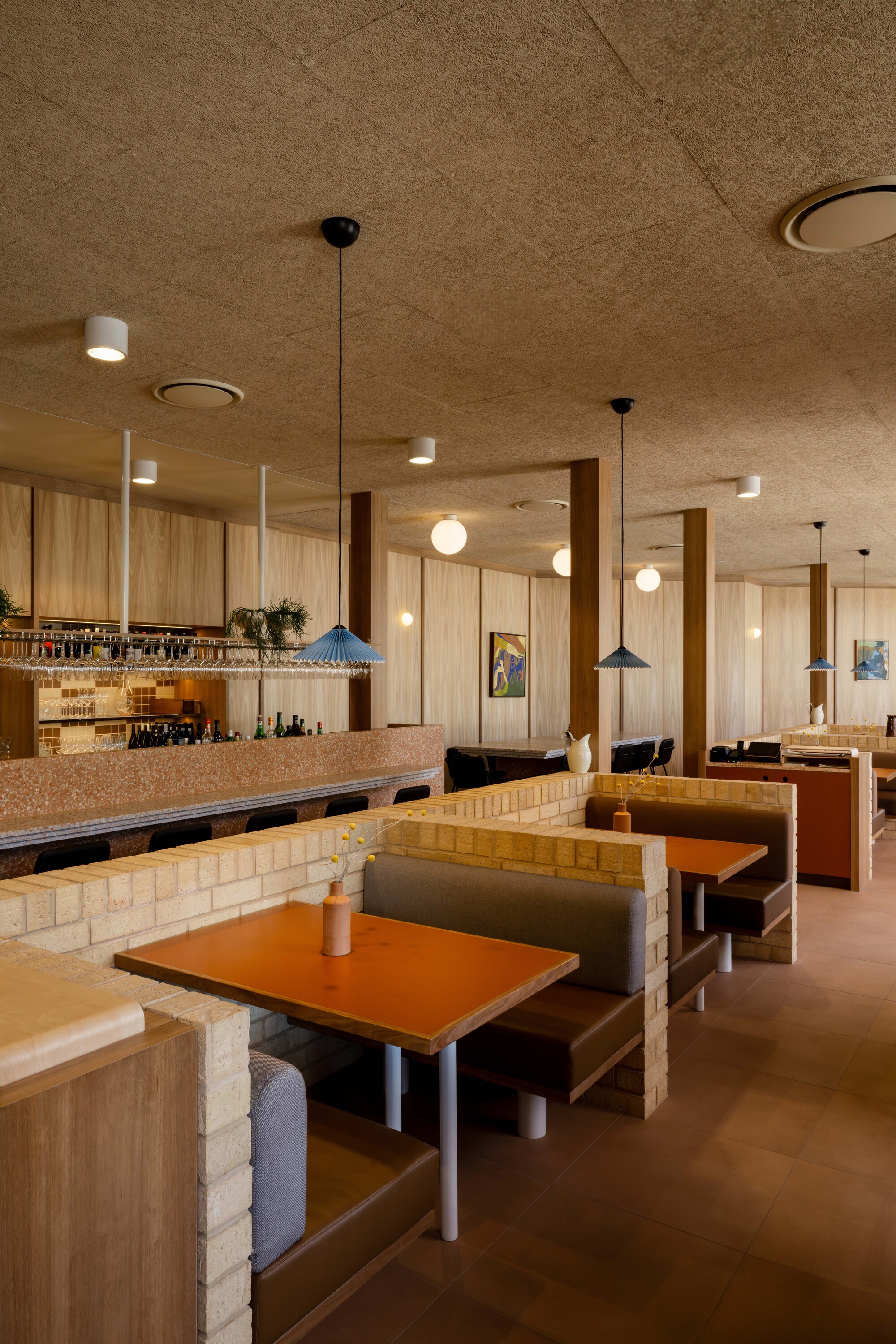 Dining area with booth seating and blonde timber partitions beneath a cork ceiling with recessed fixtures