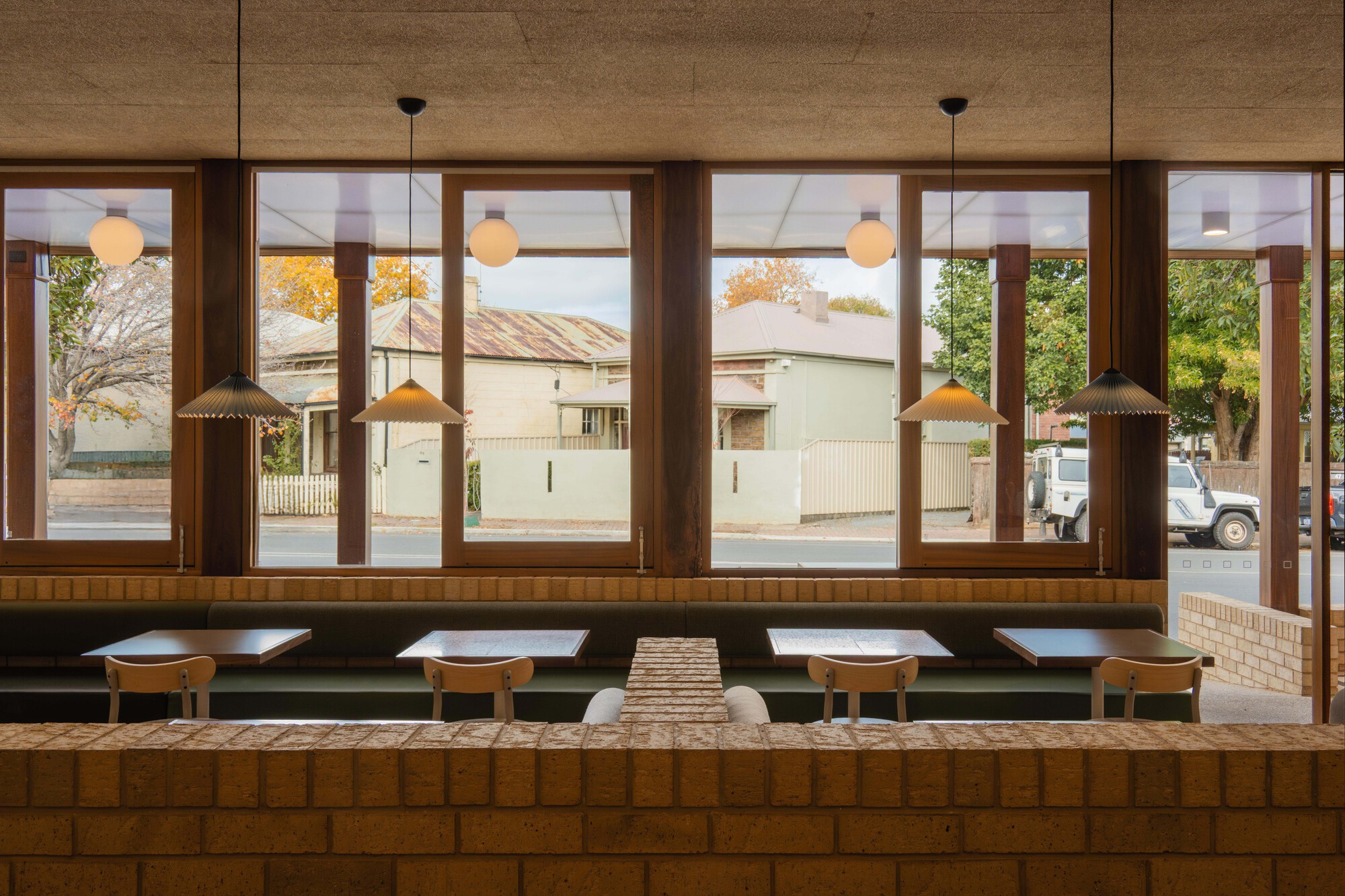 Banquette seating along timber-framed glazing overlooking a residential street in afternoon light