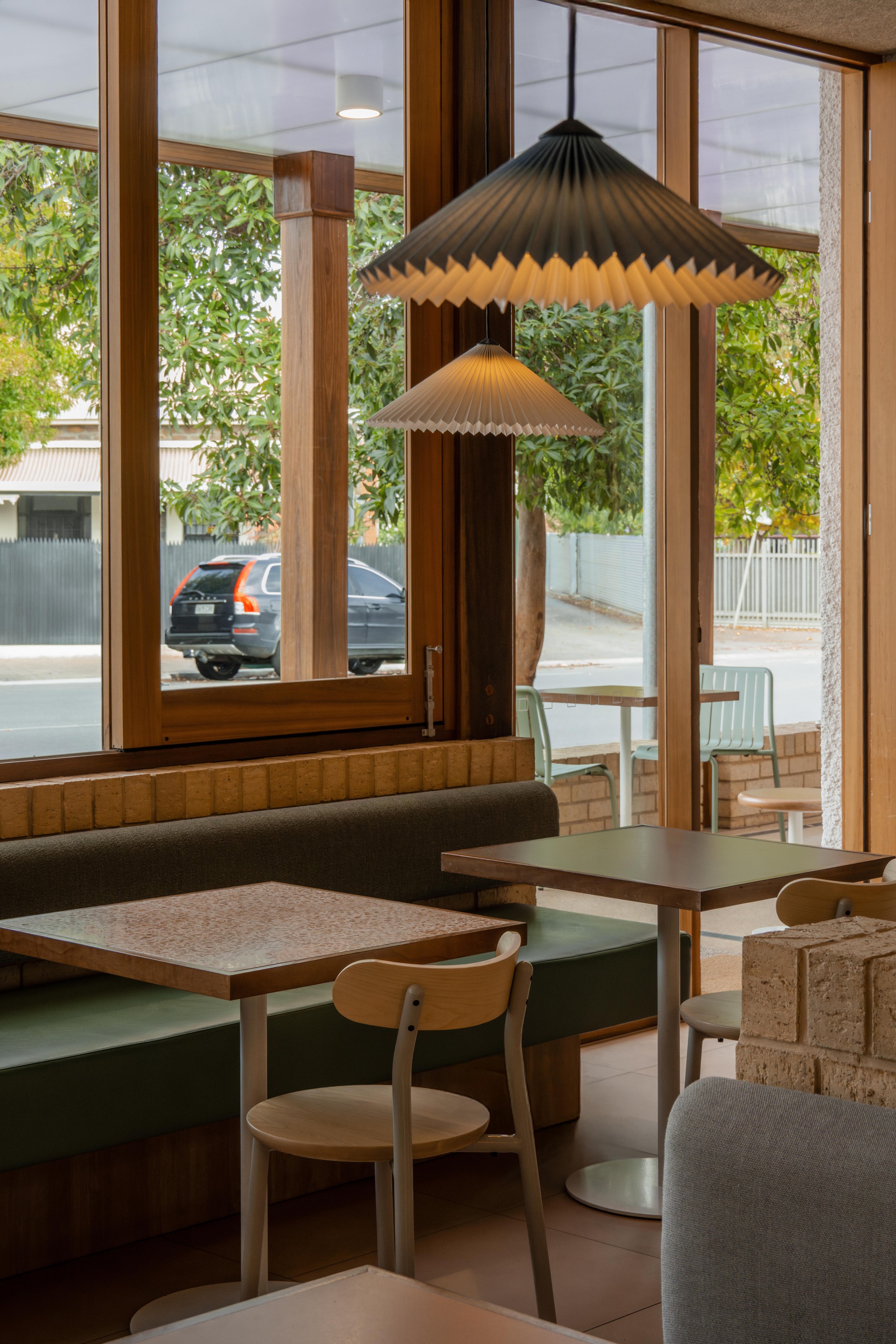 Window corner booth with pleated pendant lamps overlooking a street with parked cars and trees