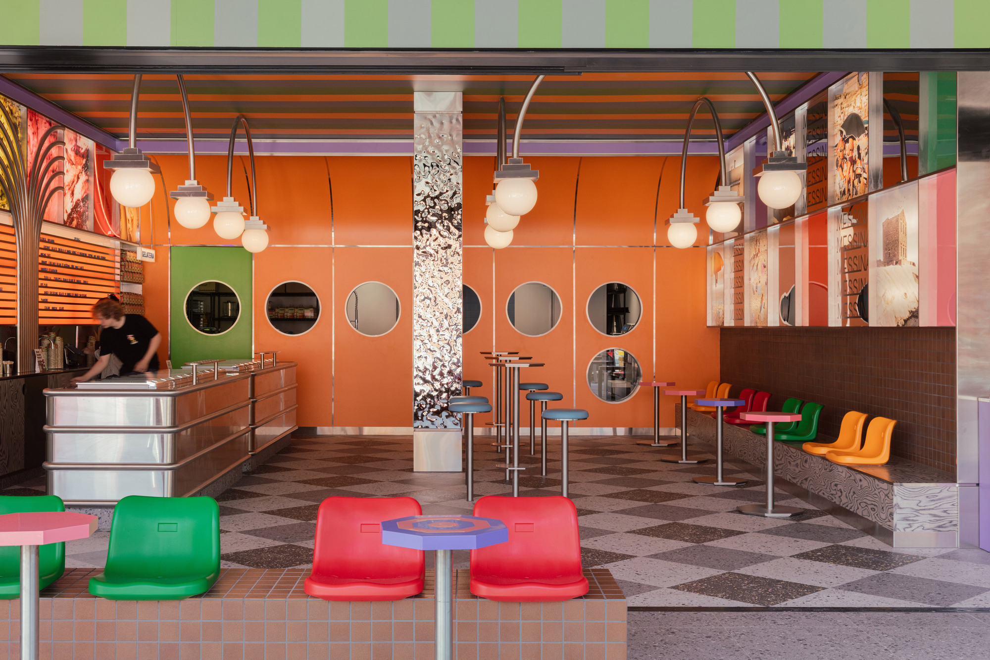 Interior cafe space with orange paneled walls punctured by circular windows and suspended globe pendant lights
