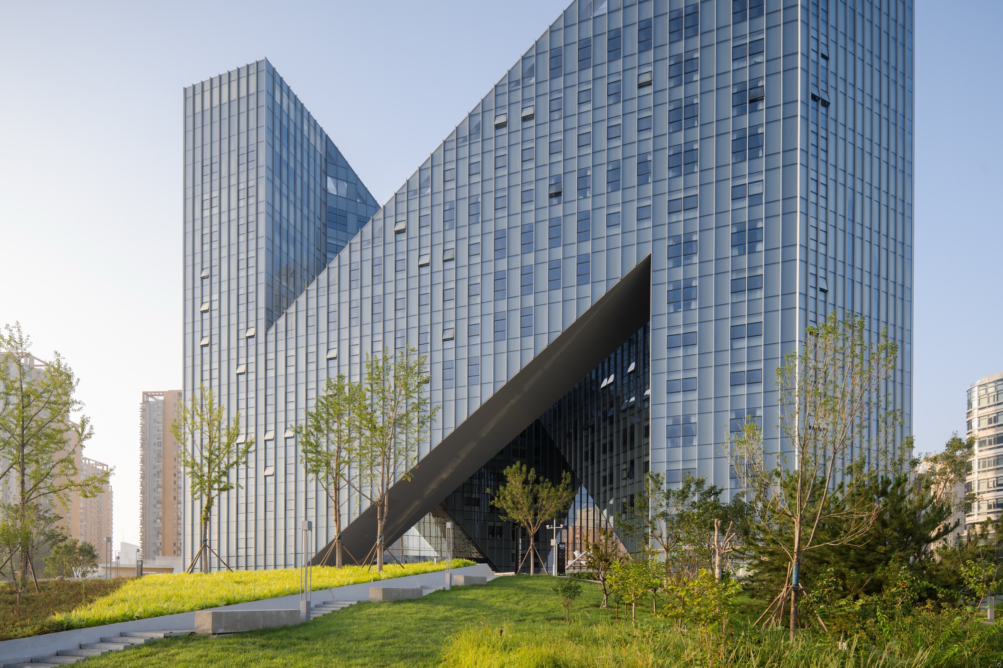 Ground-level view of the glass curtain wall facade with angled canopy over landscaped lawn