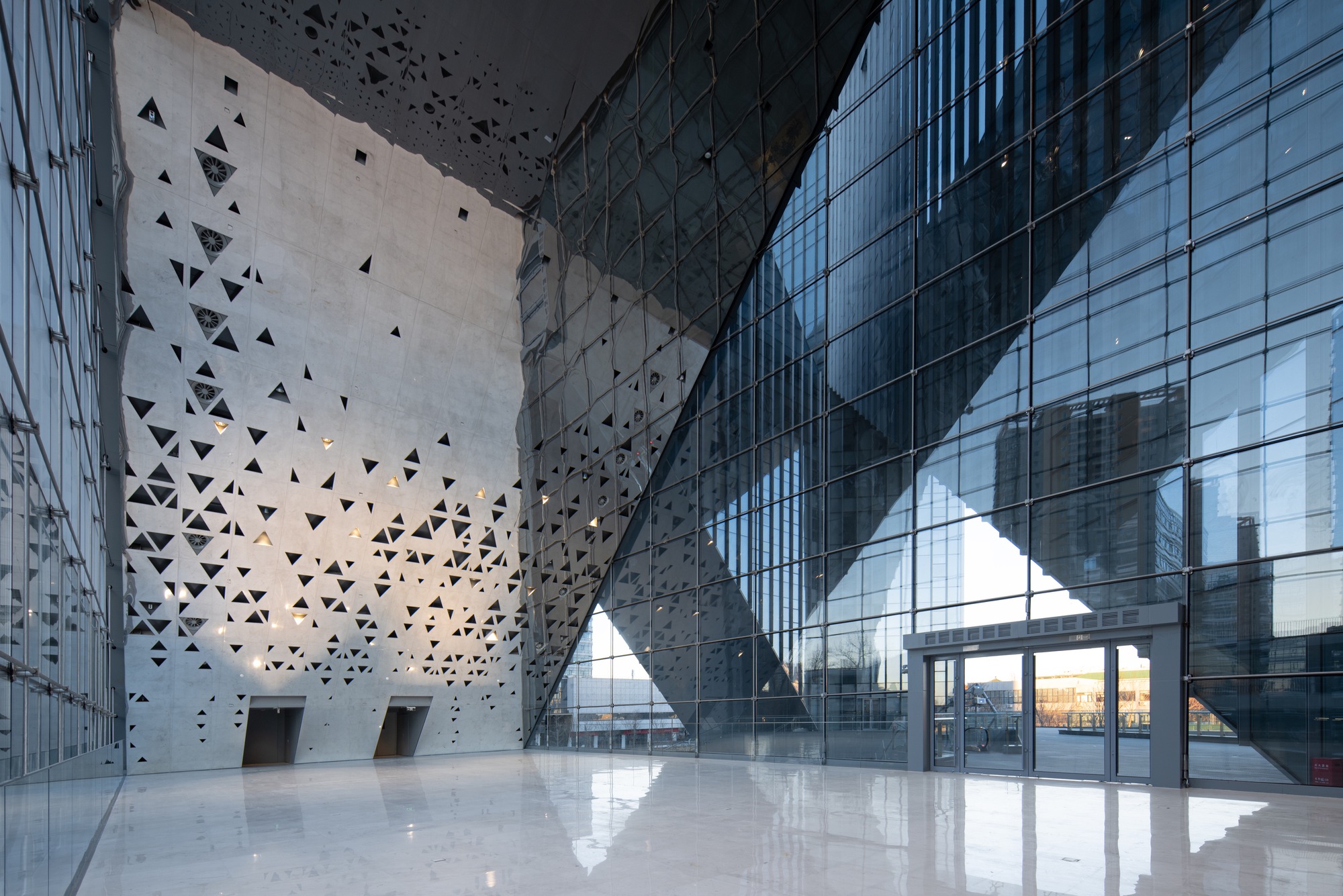 Glazed lobby with perforated concrete walls and triangular apertures in afternoon light